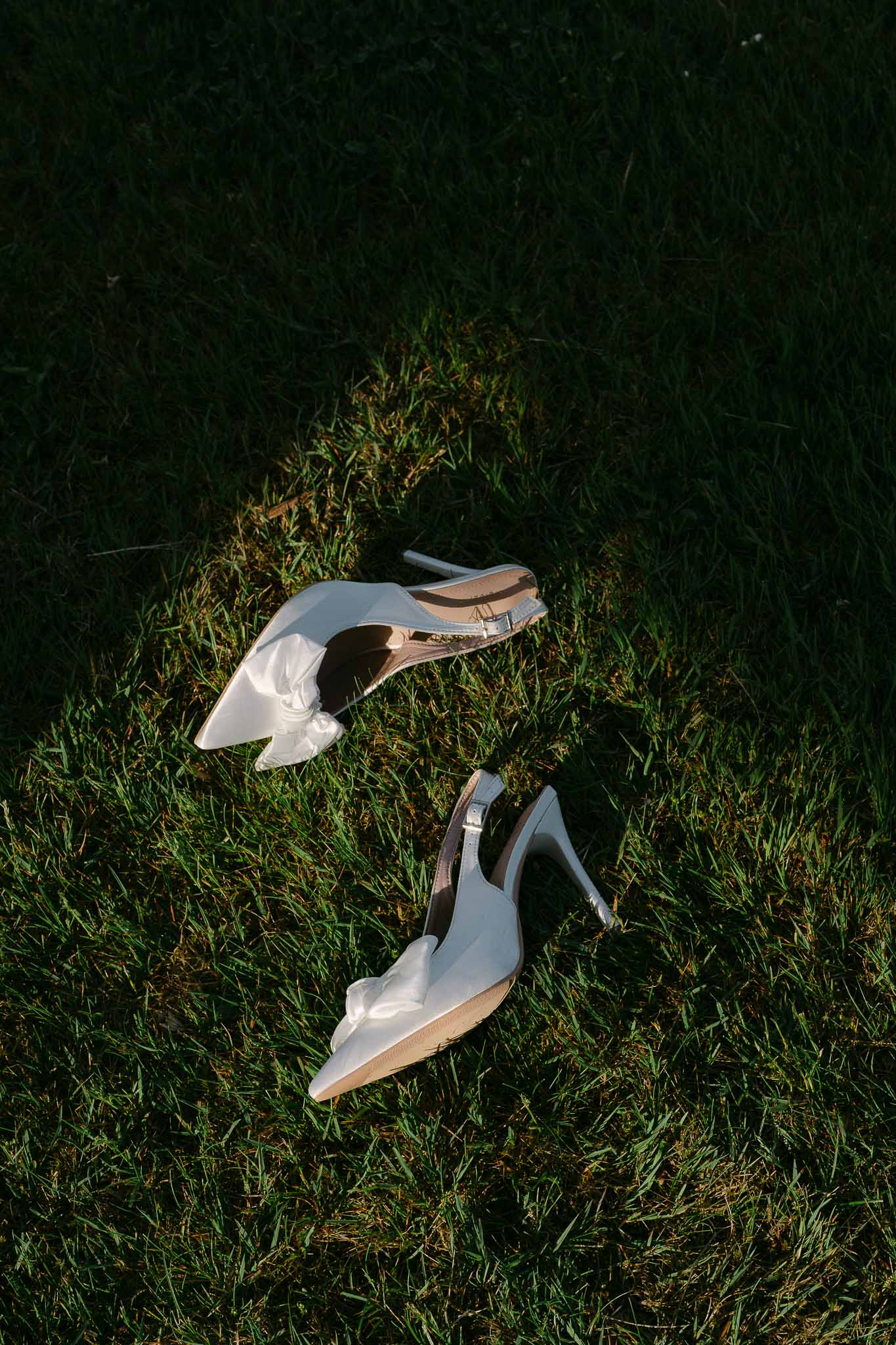 White bridal heels with ankle straps arranged on grass in outdoor flat lay composition