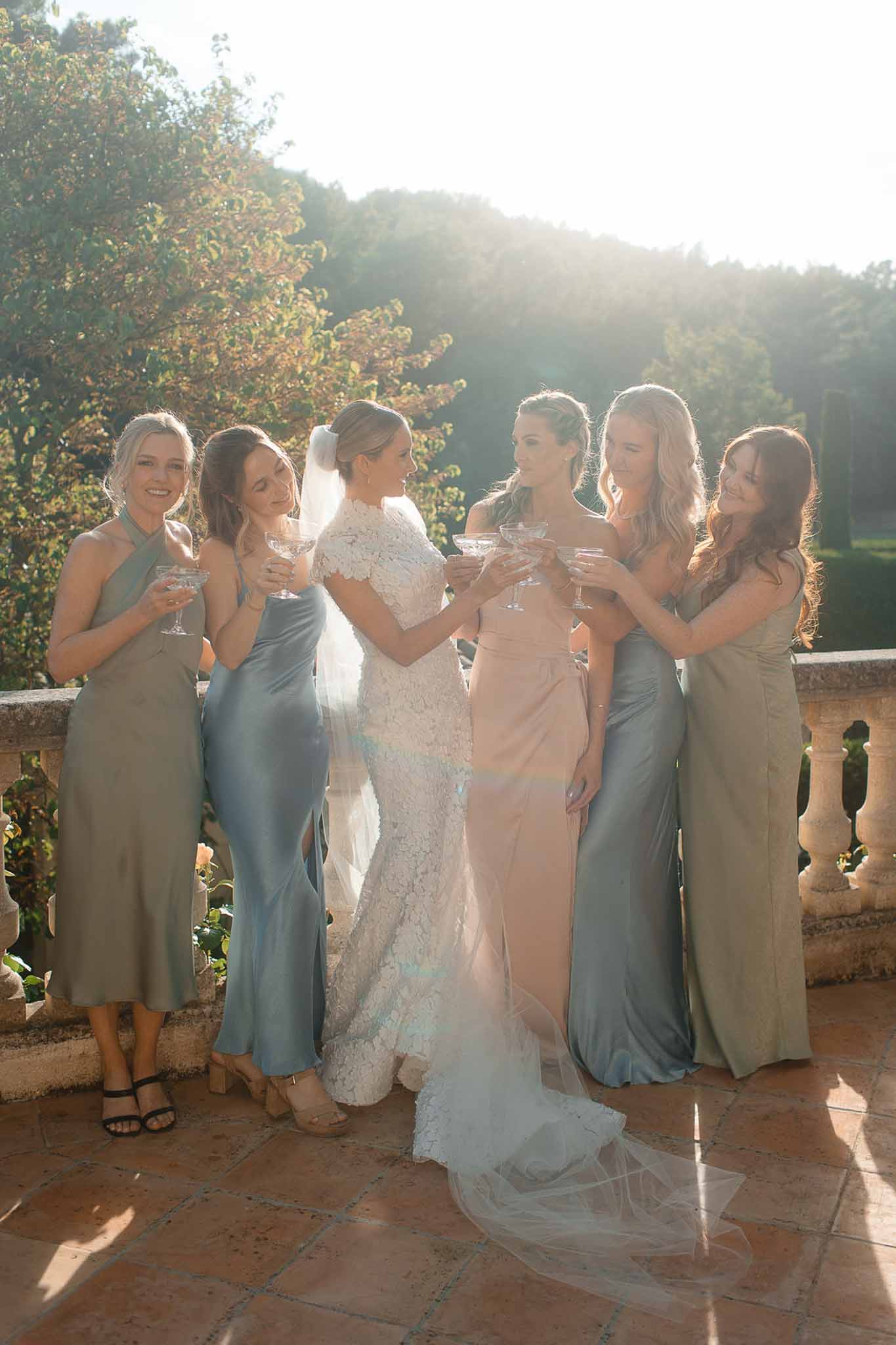 Bride and bridesmaids with champagne flutes on stone terrace overlooking forested hillside