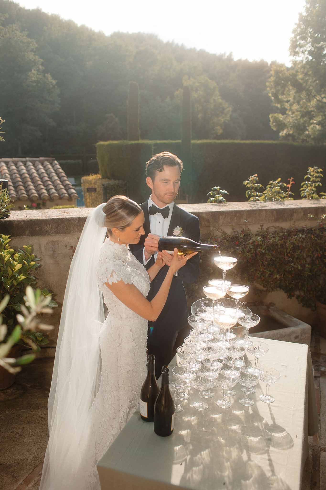 Bride and groom pouring champagne tower ceremony on outdoor terrace at Mediterranean villa reception