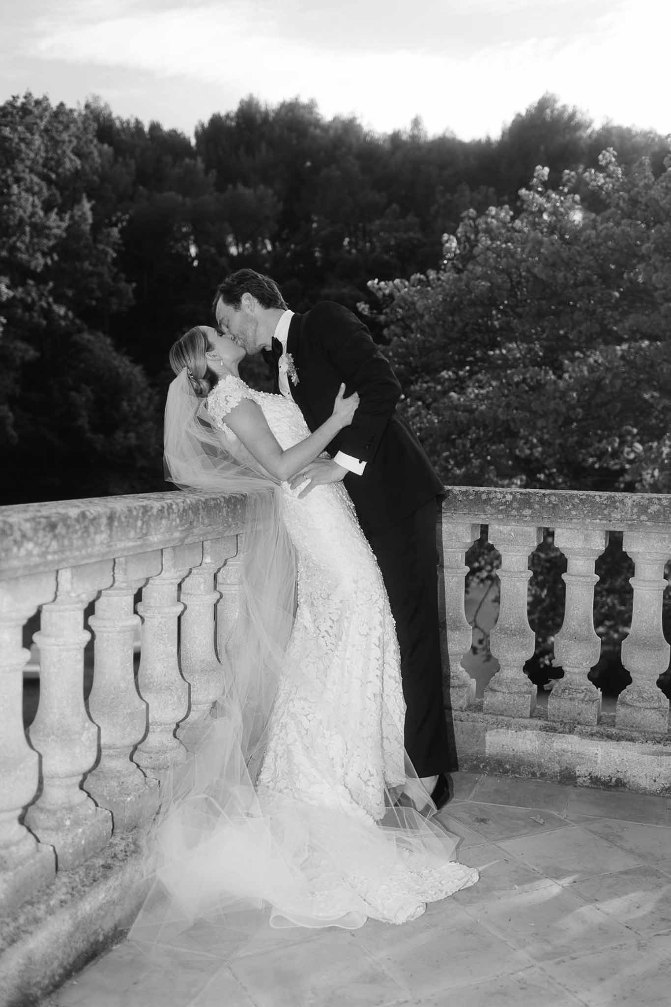 Wedding couple kissing on stone terrace overlooking formal gardens in black and white portrait