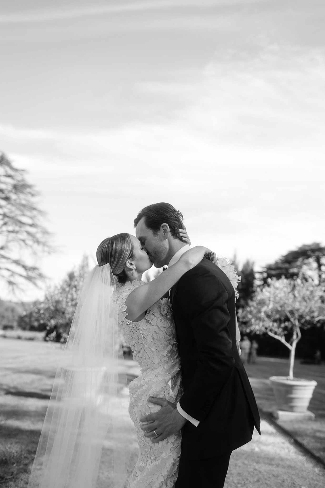 Newlywed couple kissing in garden setting during wedding day portrait session