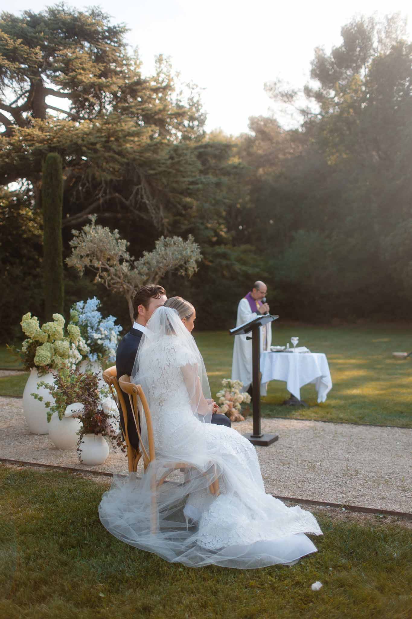 Outdoor wedding ceremony in garden setting with bride in ivory gown and groom in navy suit