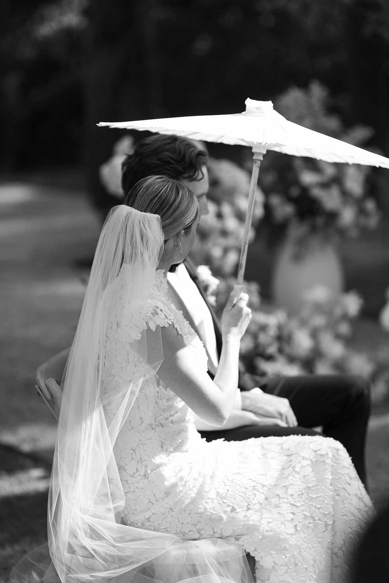 Bride and groom seated together during outdoor ceremony with parasol