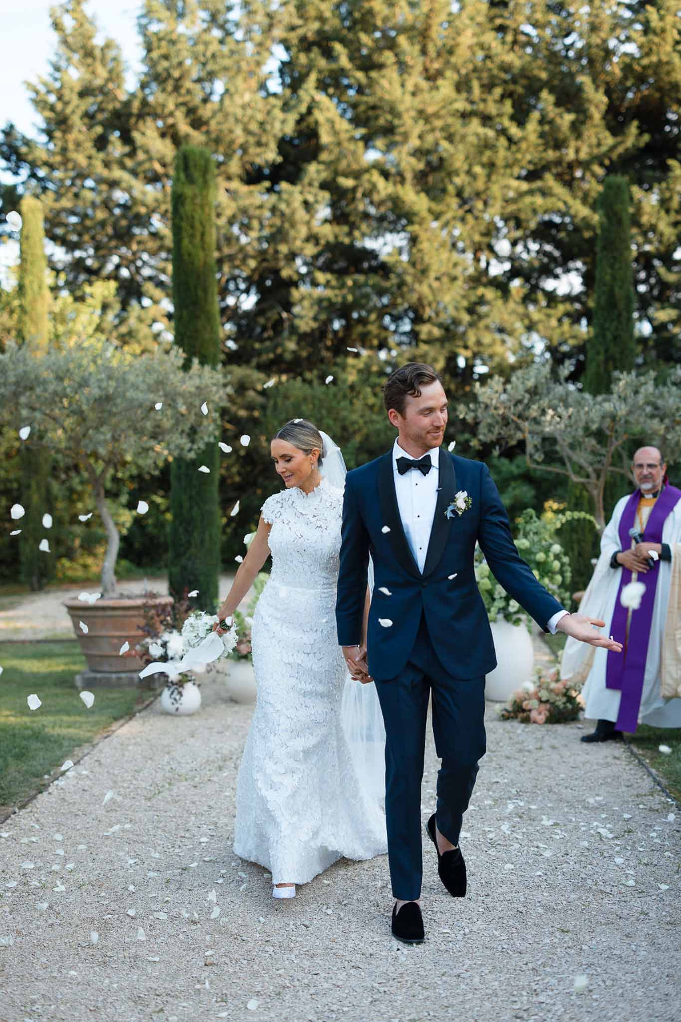 Bride and groom walking down ceremony aisle with flower petals at Mediterranean garden wedding venue