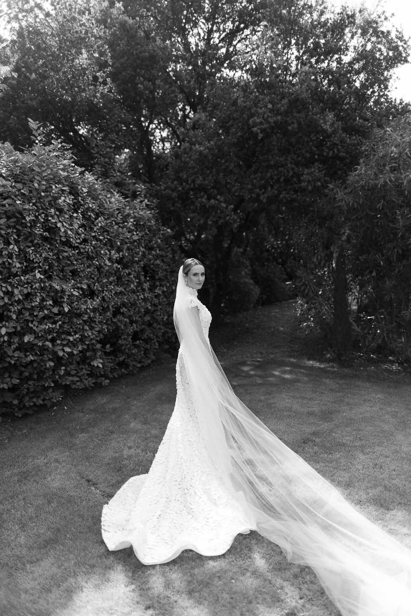 Bride in embellished gown with dramatic veil in formal garden setting