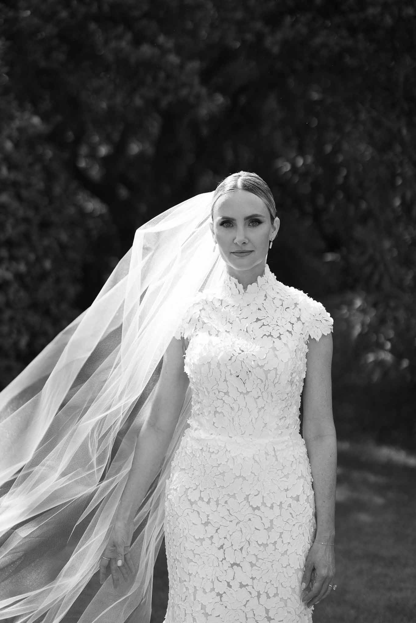 Black and white bridal portrait of bride in lace wedding dress with flowing veil outdoors