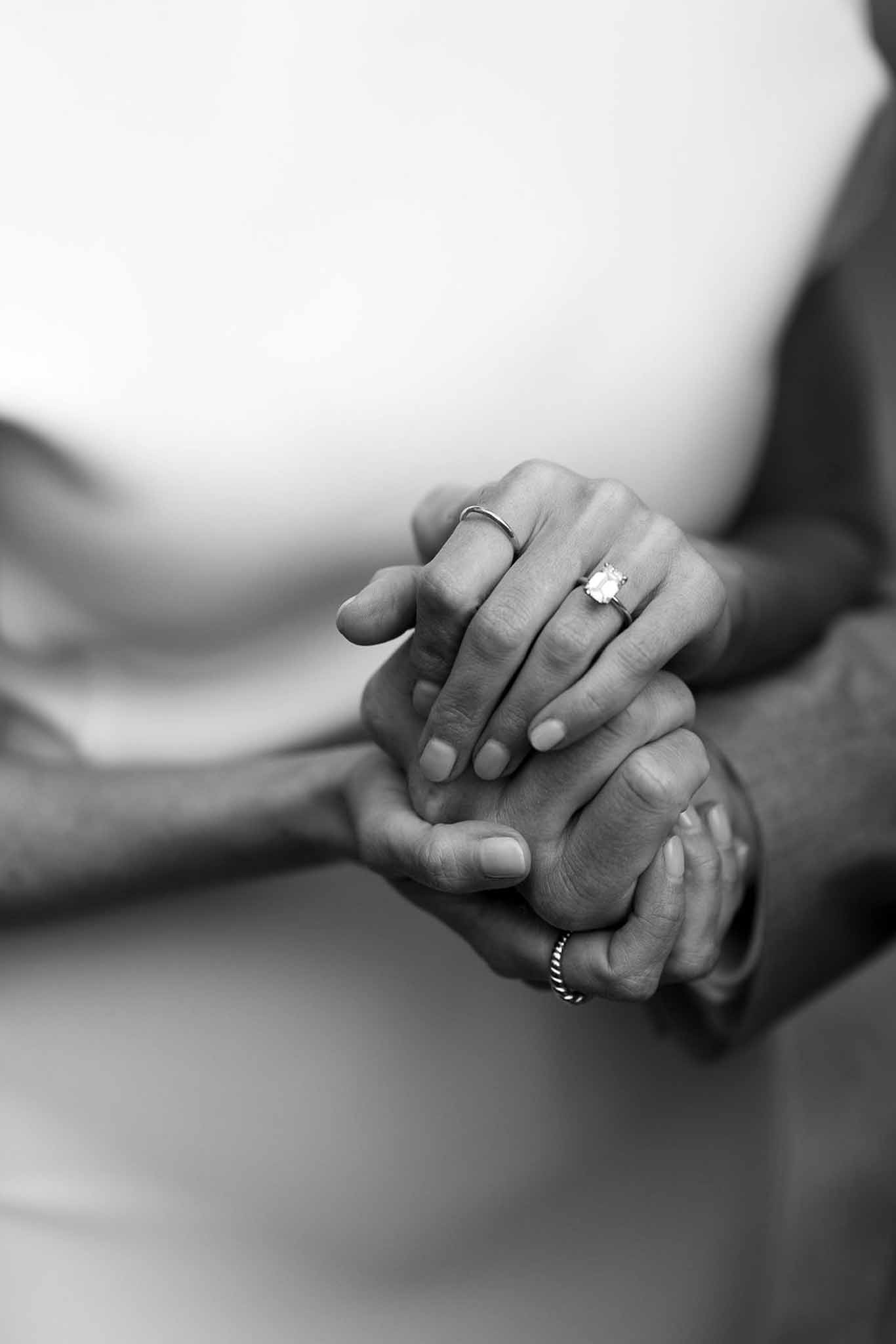 Black and white close-up of bride and groom's hands showing wedding rings and engagement ring