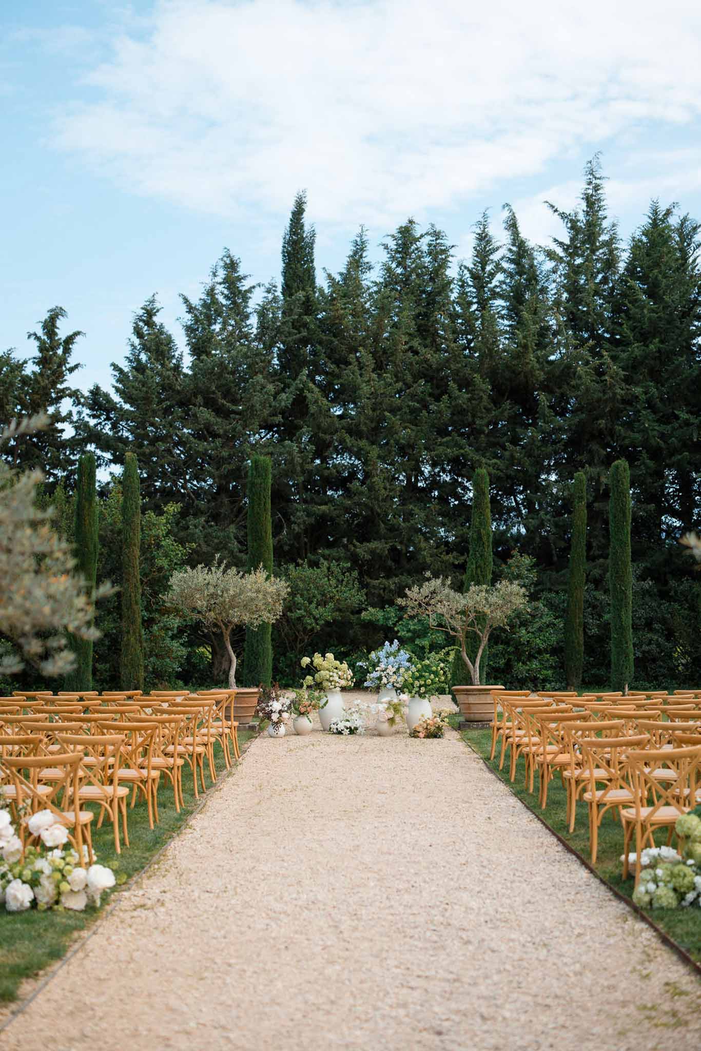 Outdoor wedding ceremony setup with wooden chairs and floral arrangements in Mediterranean garden setting