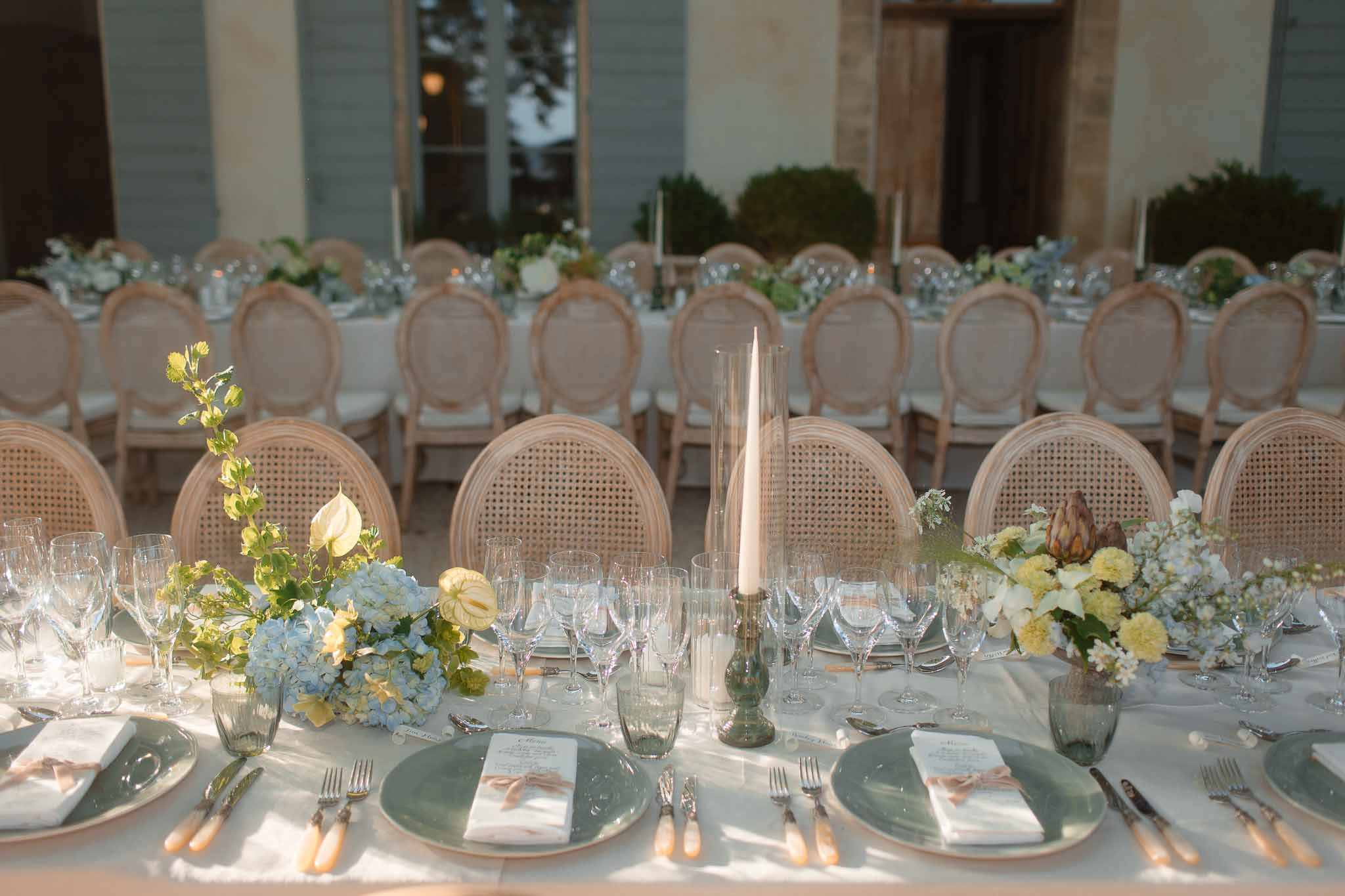 Elegant outdoor reception tablescape with sage chargers and floral centerpieces in modern courtyard setting