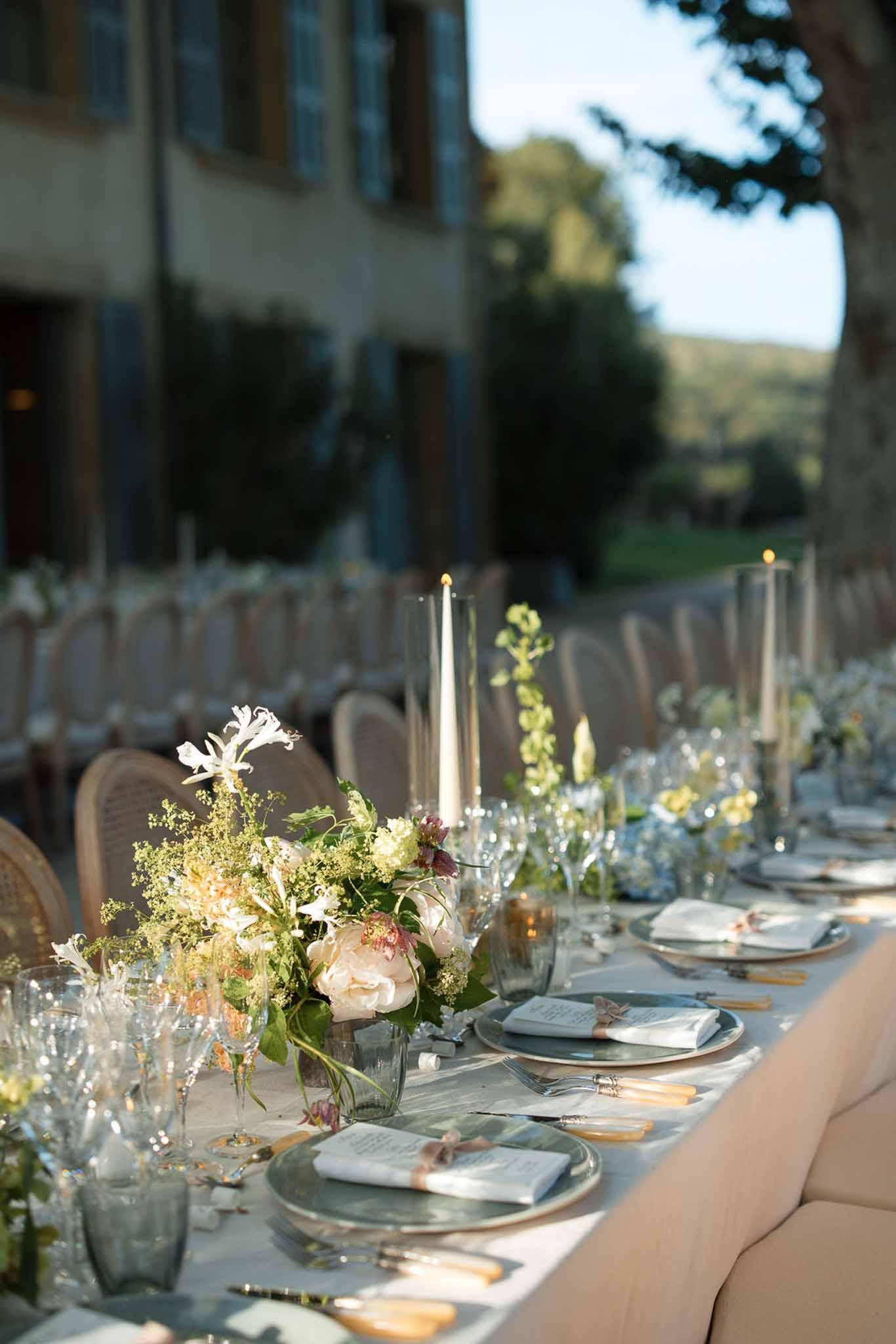 Reception table setting with sage plates, gold flatware, and white floral arrangements at outdoor wedding venue