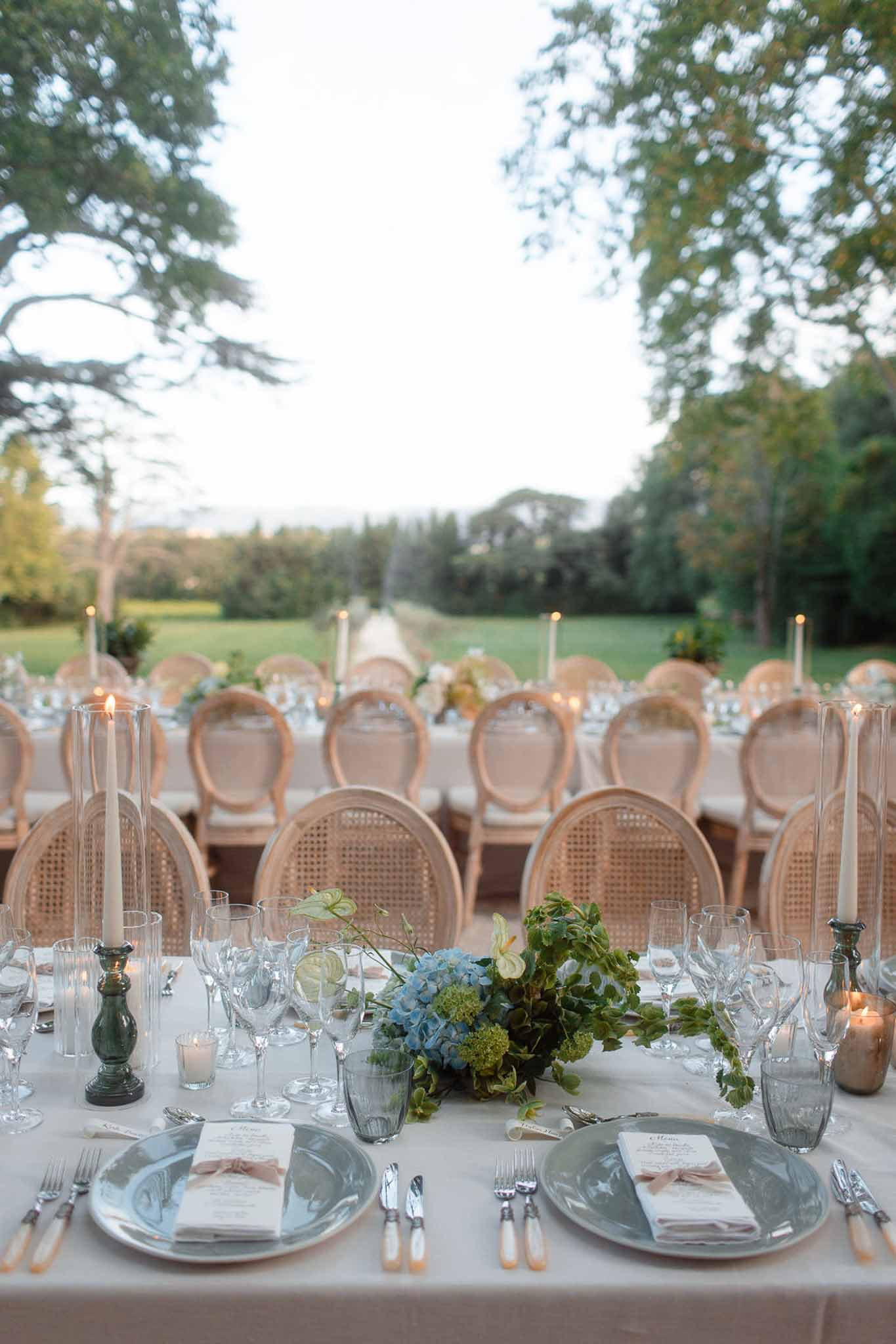 Elegant outdoor reception table with blue and ivory place settings in estate garden