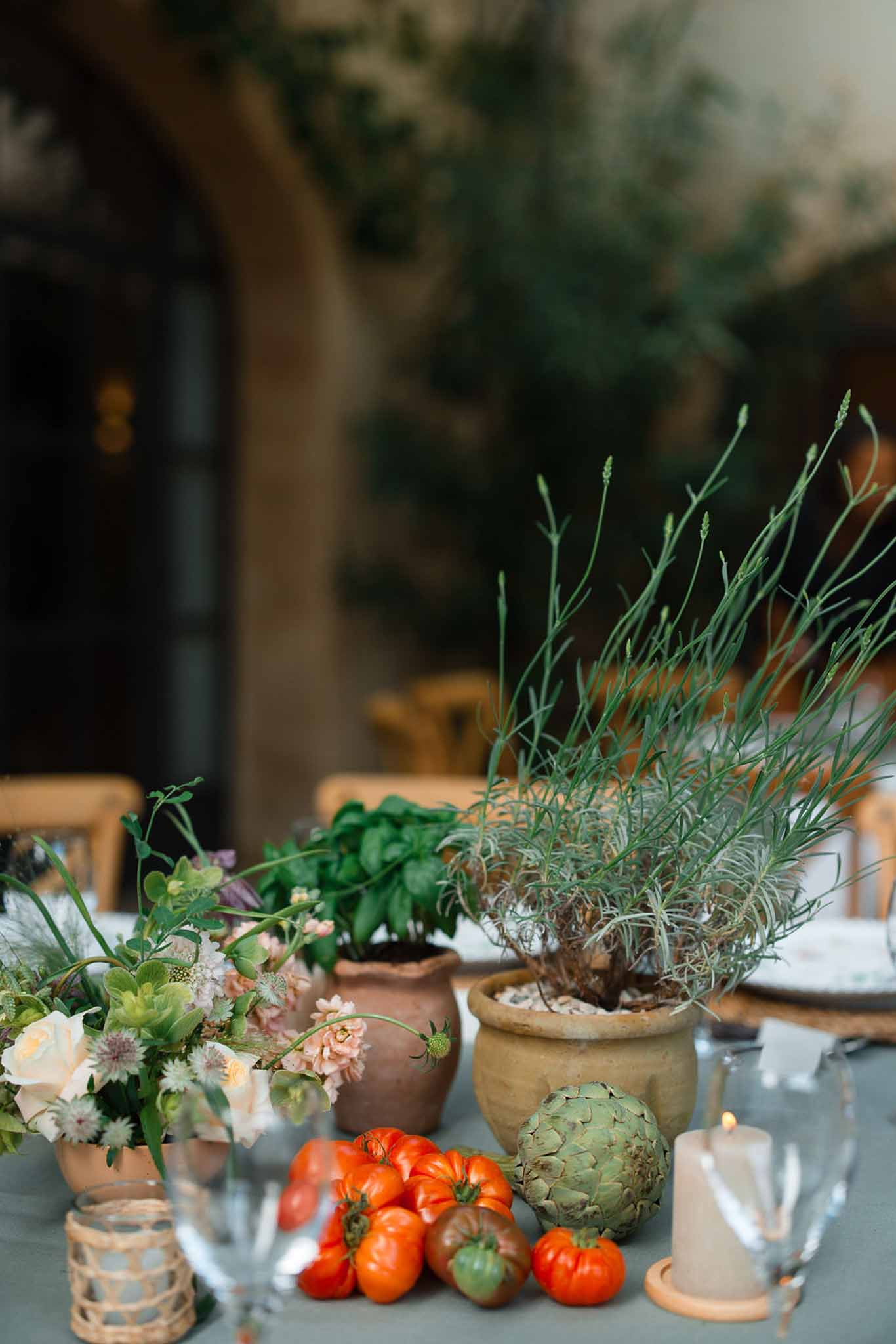Mediterranean-inspired reception table with terracotta pots, herbs, and produce at stone courtyard venue