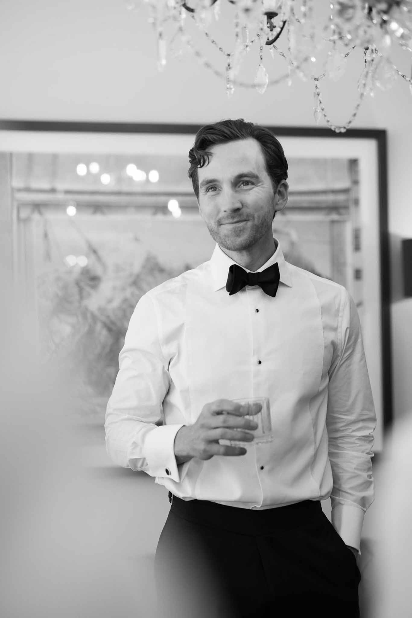 Groom in black-tie attire holding glass during wedding reception at elegant indoor venue