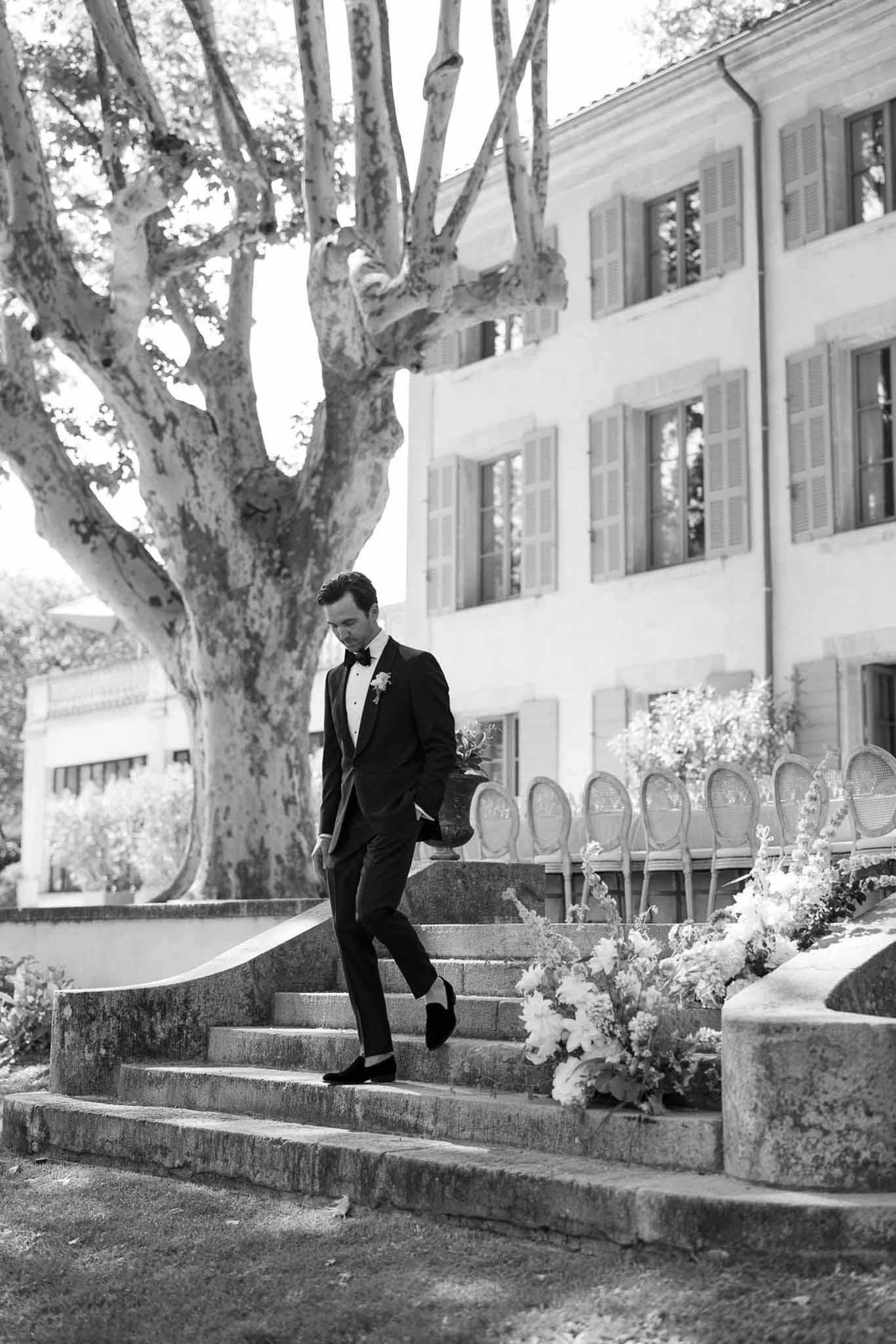 Groom in black tuxedo on stone staircase at classical courtyard wedding venue