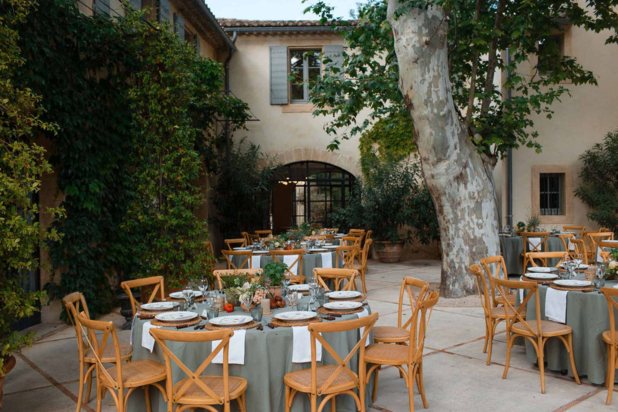 Reception tables with sage linens in historic European courtyard with stone architecture and ivy-covered walls
