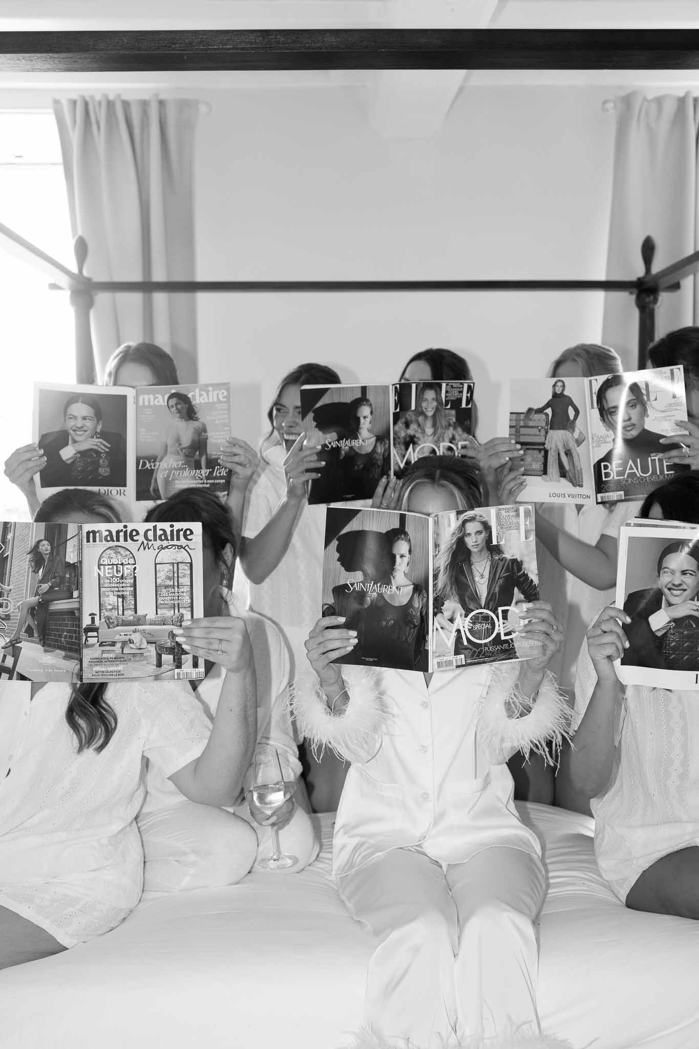 Black-and-white photo of bride and bridesmaids in white robes holding French magazines over their faces
