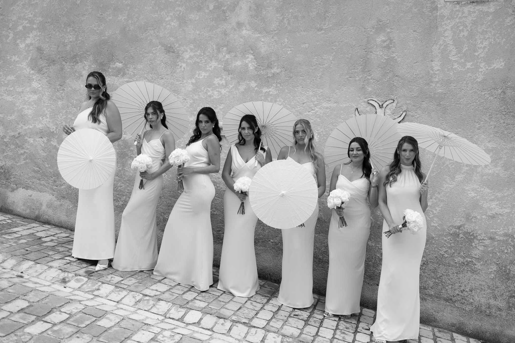 Black and white portrait of seven bridesmaids in slip dresses holding parasols and peony bouquets