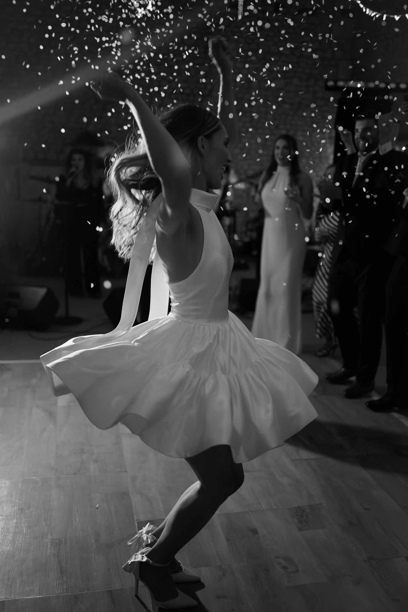 Black and white bride spinning in short halter dress with confetti cannon burst on wooden dance floor