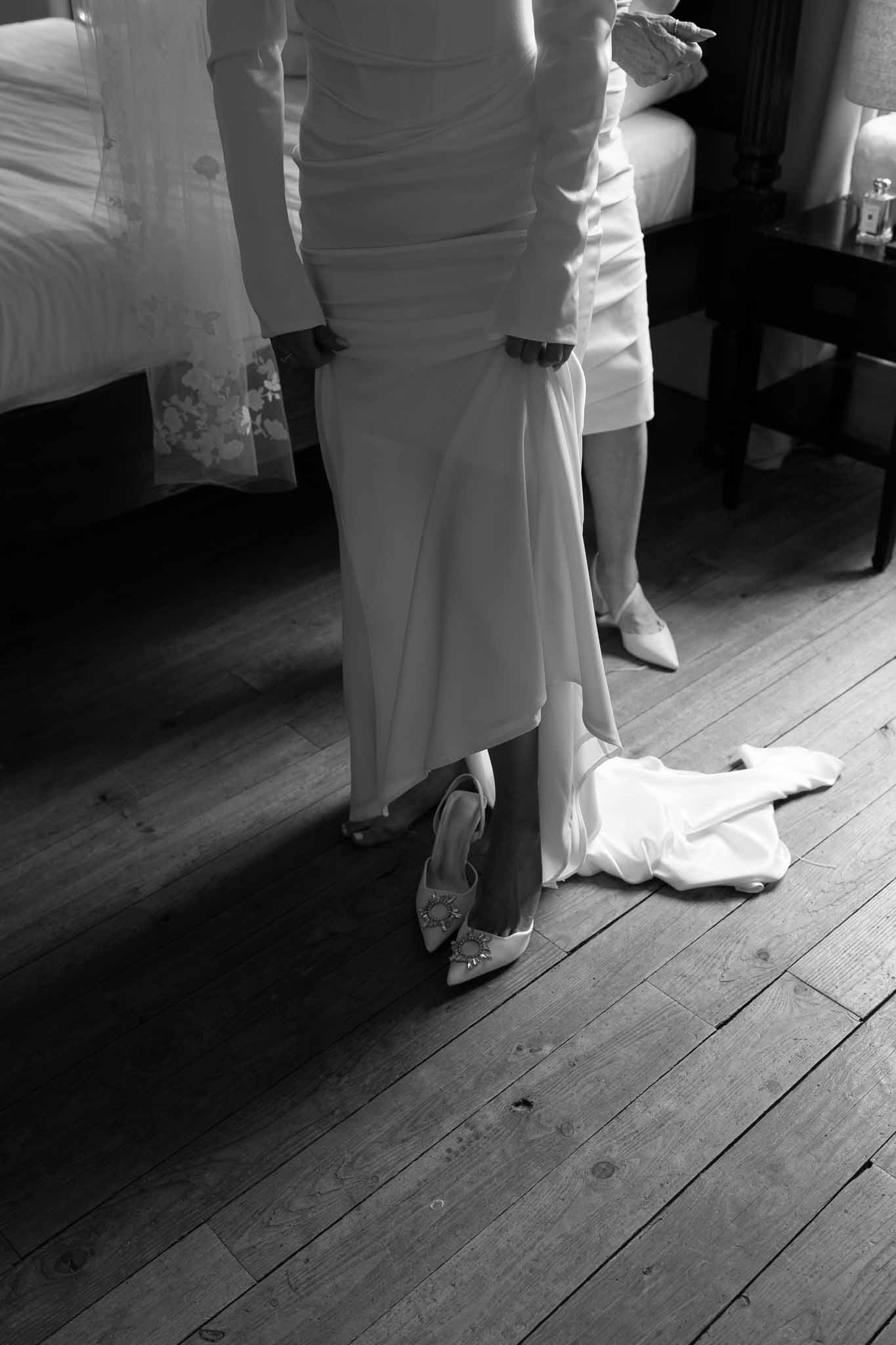 Black and white waist-down shot of bride in fitted gown with jeweled slingback heels on wooden floor