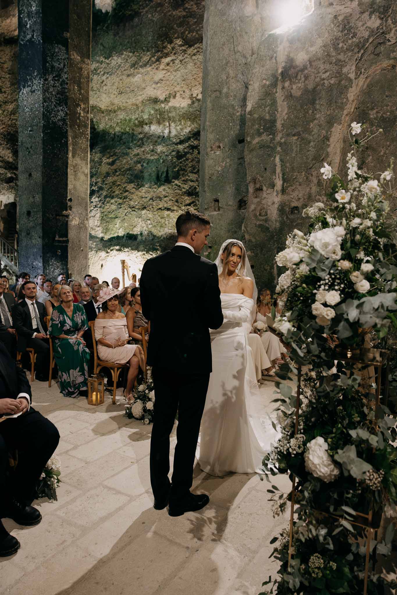 Wedding ceremony inside underground cave with couple at altar and floral arrangement on gold stand