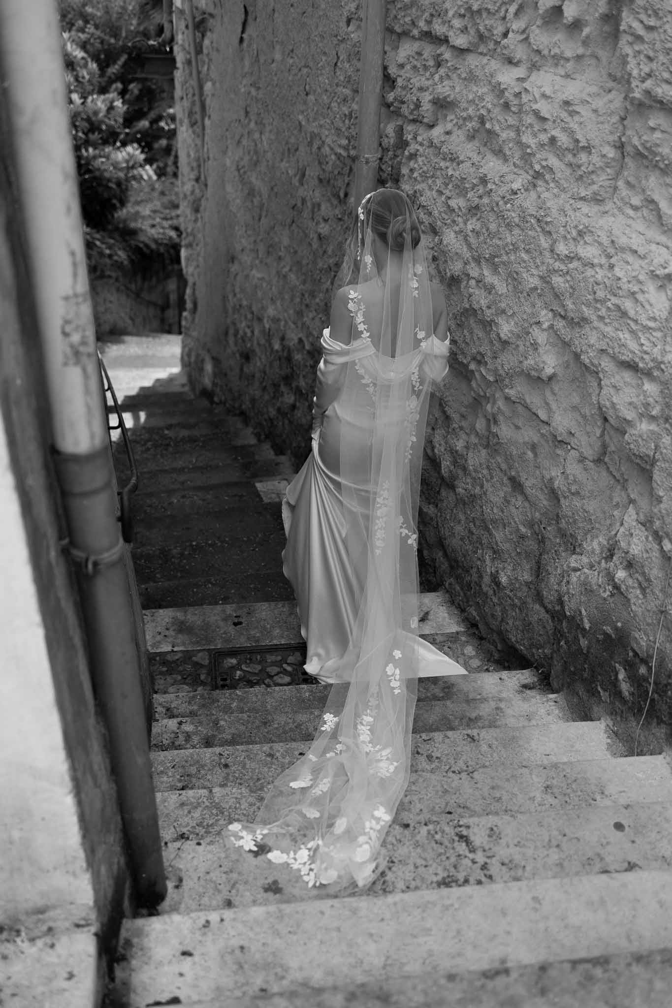 Overhead view of bride descending stone stairs with lace-trimmed cathedral veil cascading full length in B&W