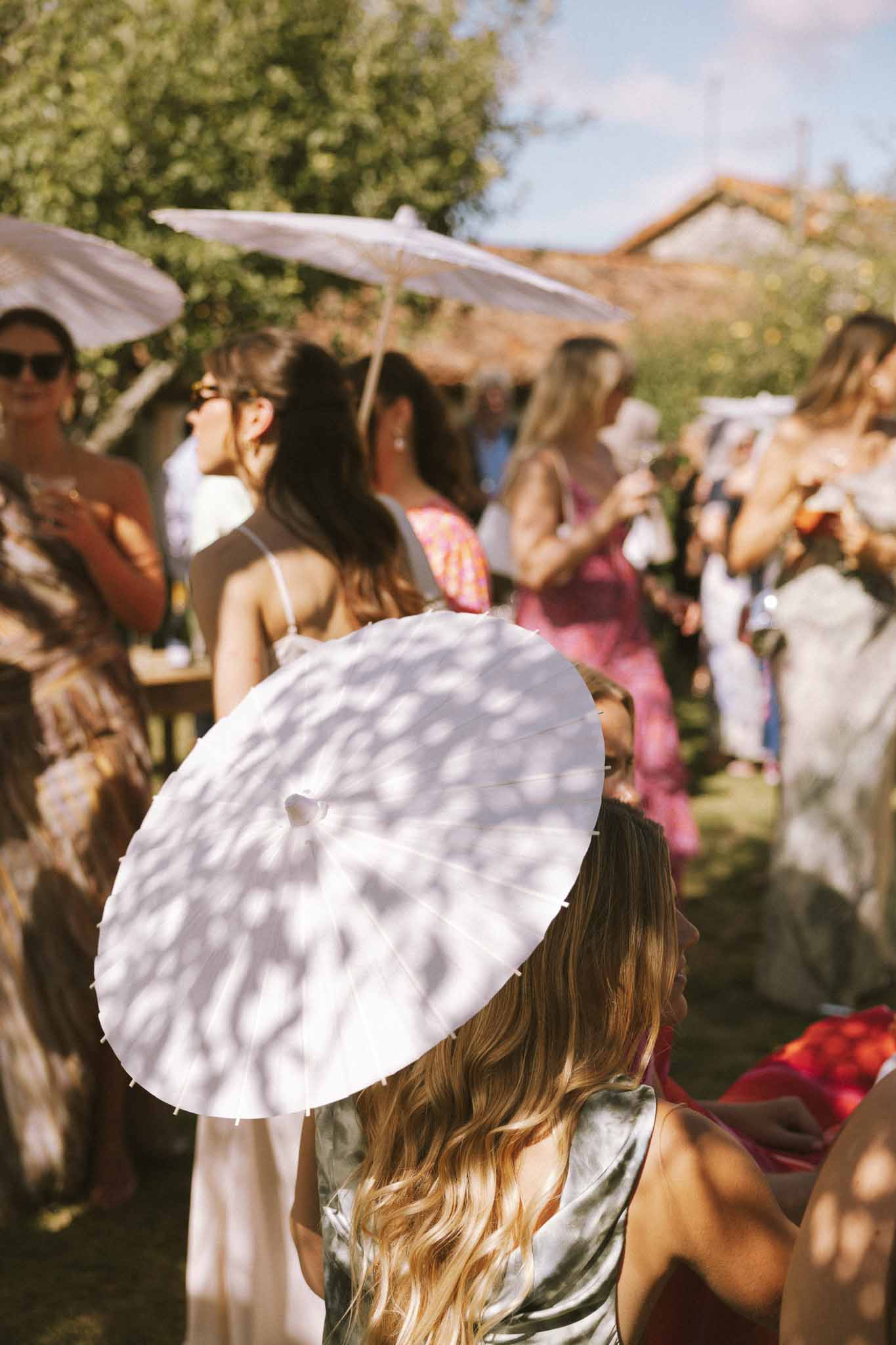 Guests mingling with white paper parasols during sunny afternoon cocktail hour on garden lawn