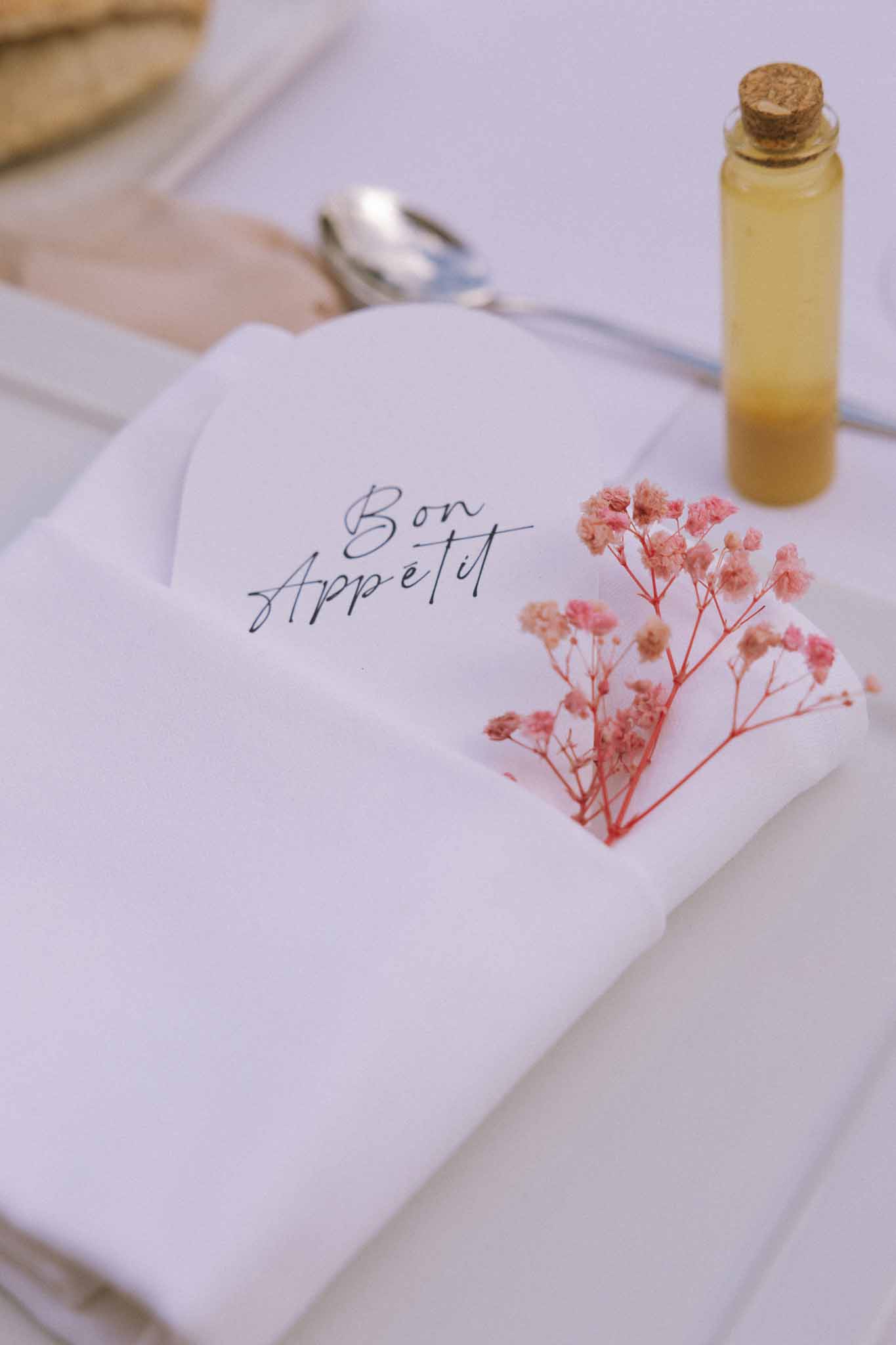 Reception place setting with Bon Appetit calligraphy card, dried pink gypsophila, and glass favour vial