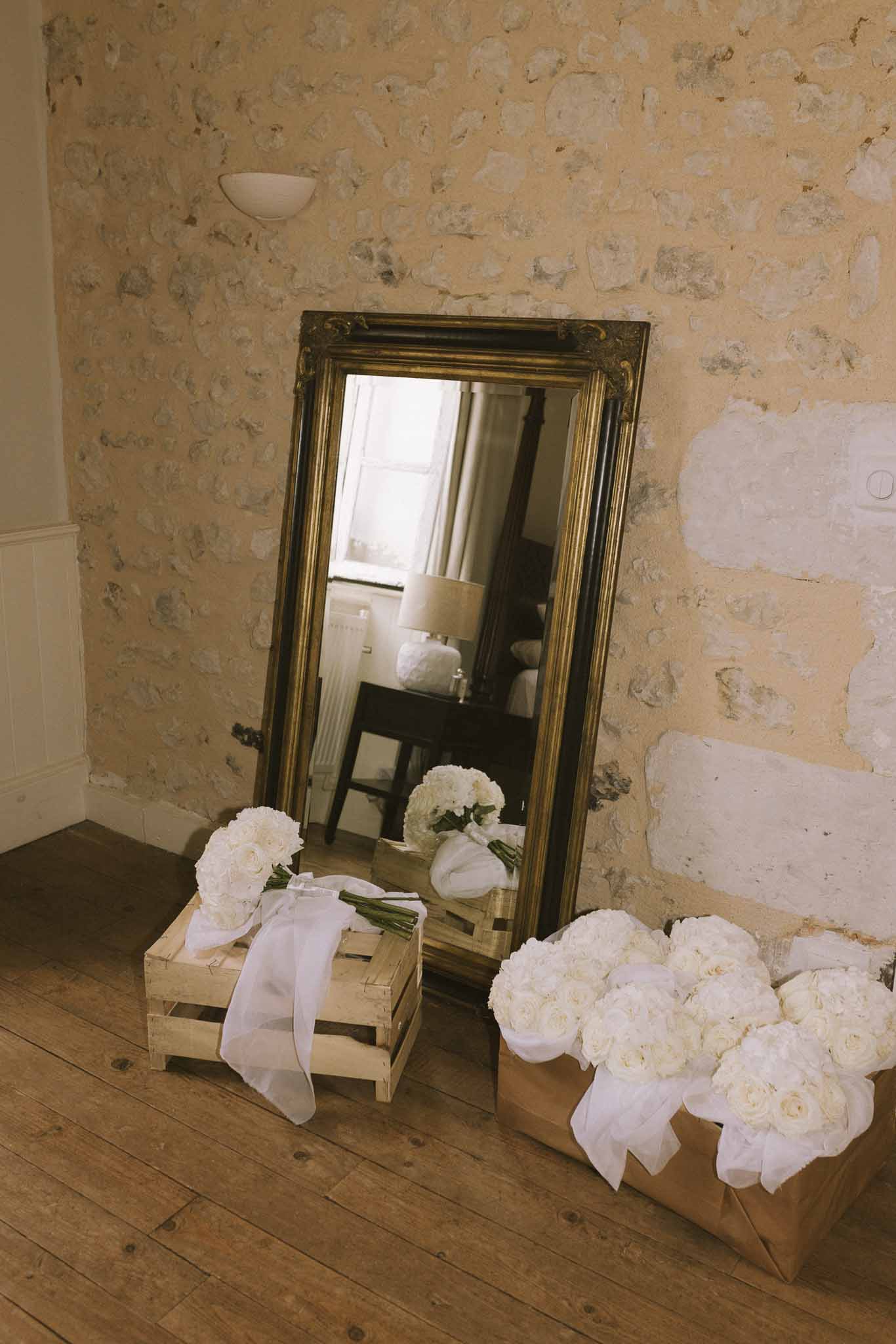White rose bouquets tied with sheer ribbon arranged on floor beside ornate gold-framed mirror in chateau interior