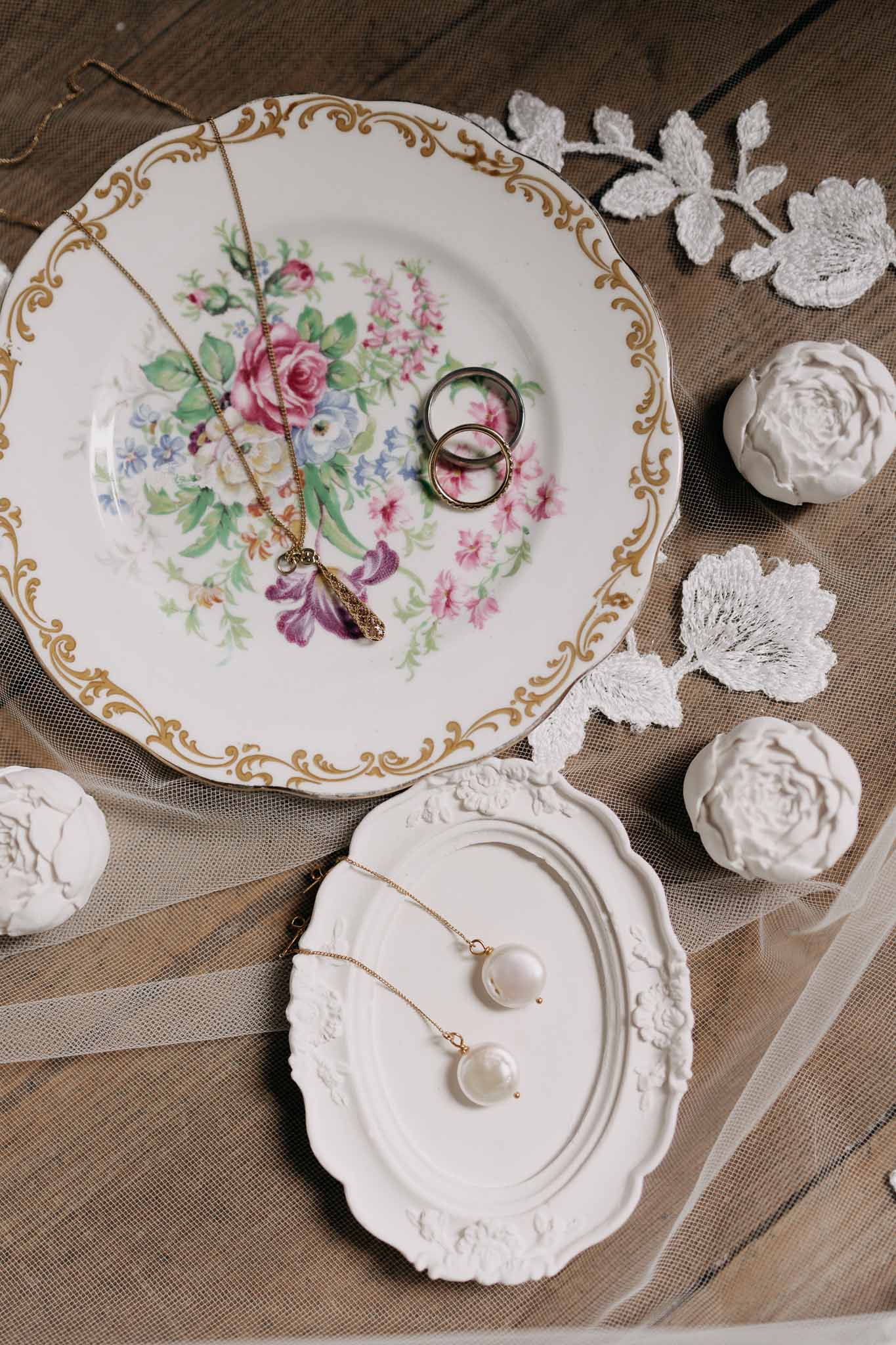 Vintage porcelain plate with gold bands and pearl necklace on ivory tulle with plaster rose accents