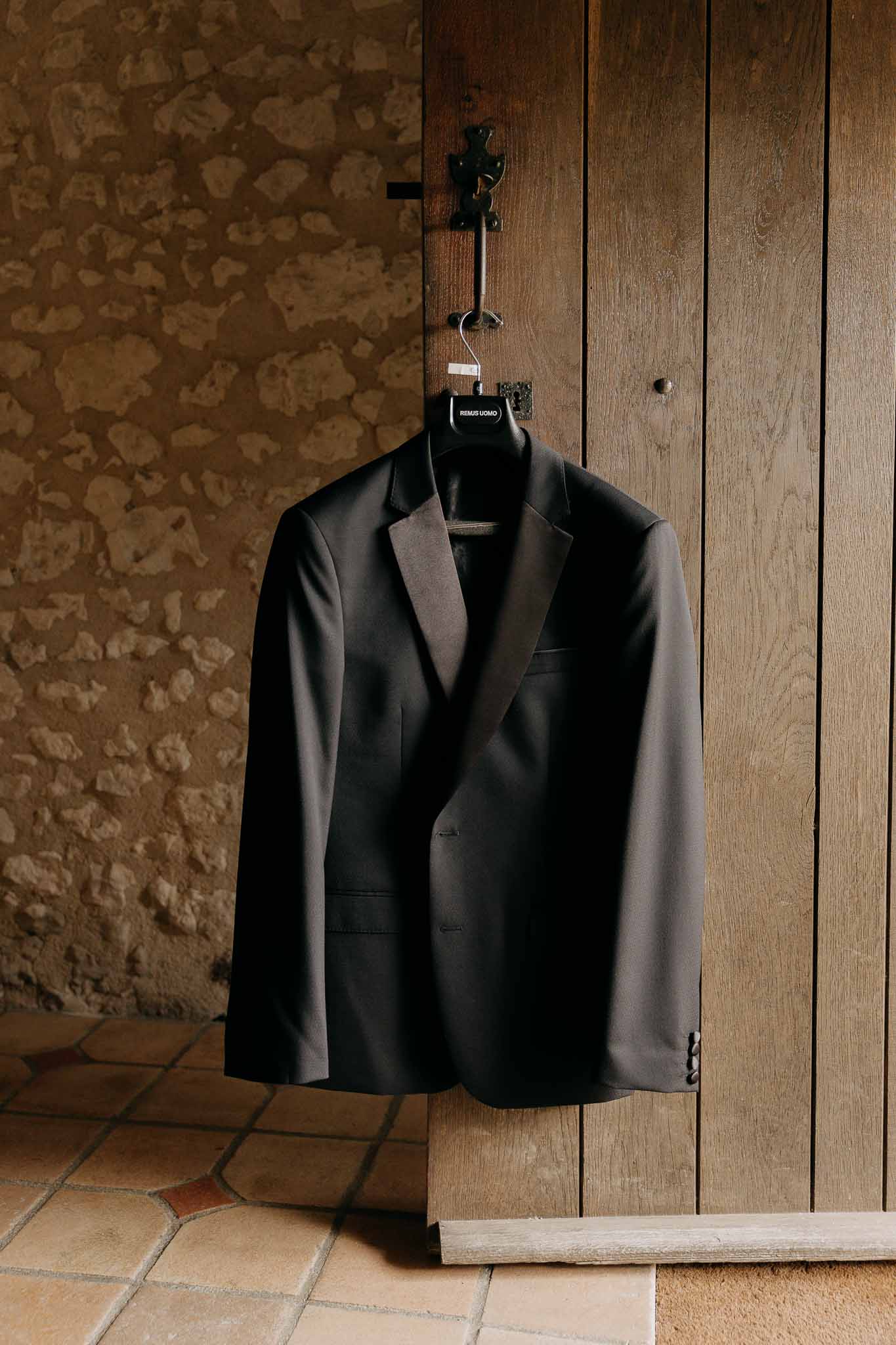 Black Remus Uomo dinner jacket hanging on iron fixture on rustic wooden door