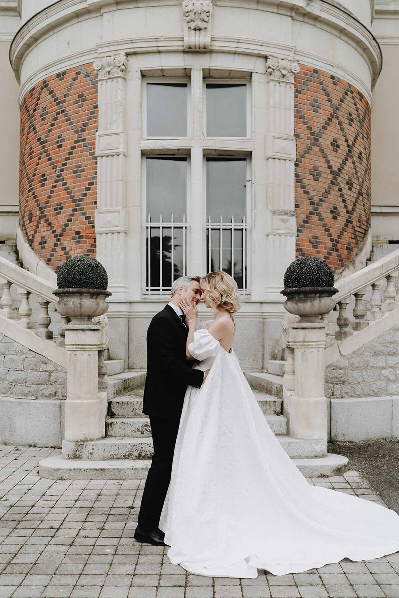 Bride and groom foreheads touching before chateau with brick turret and double staircase