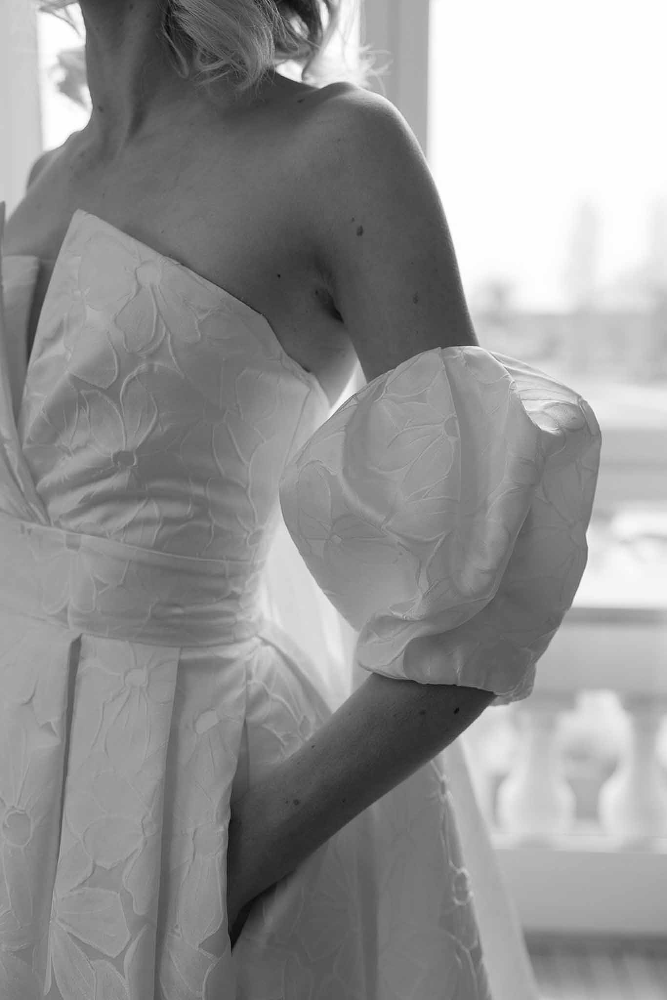 Black and white close-up of strapless floral jacquard gown with detachable puff sleeve and bow sash at waist