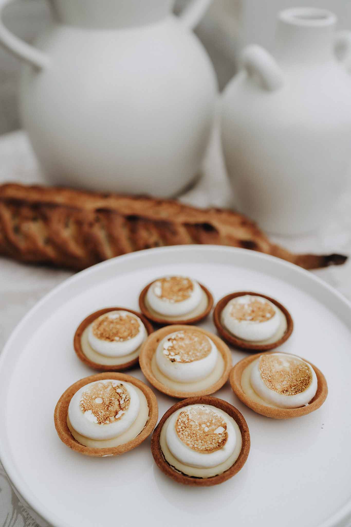 Seven mini lemon meringue tarts with torched golden meringue arranged on a round white ceramic plate