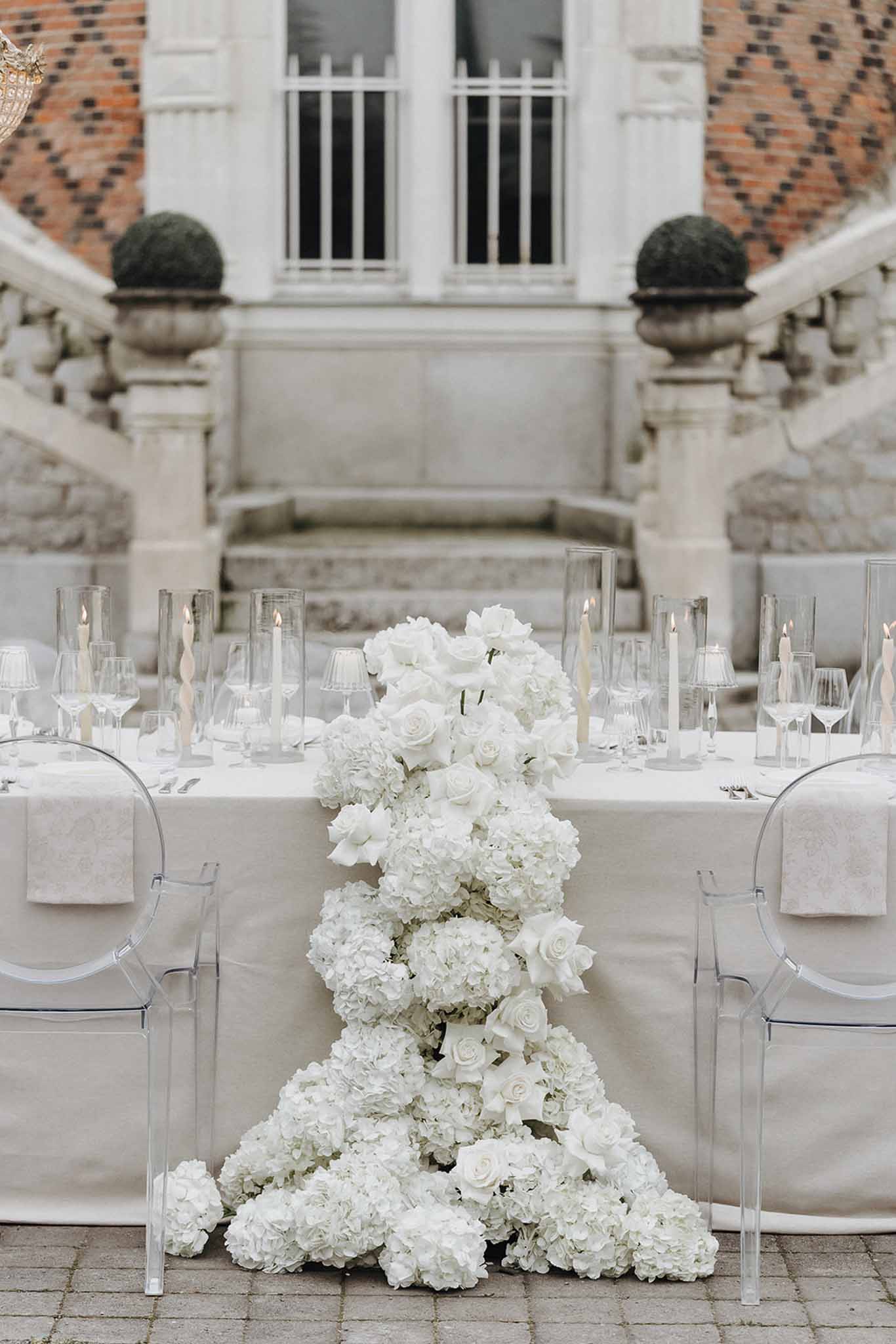 Sweetheart table with cascading white hydrangea and rose runner before chateau double staircase courtyard