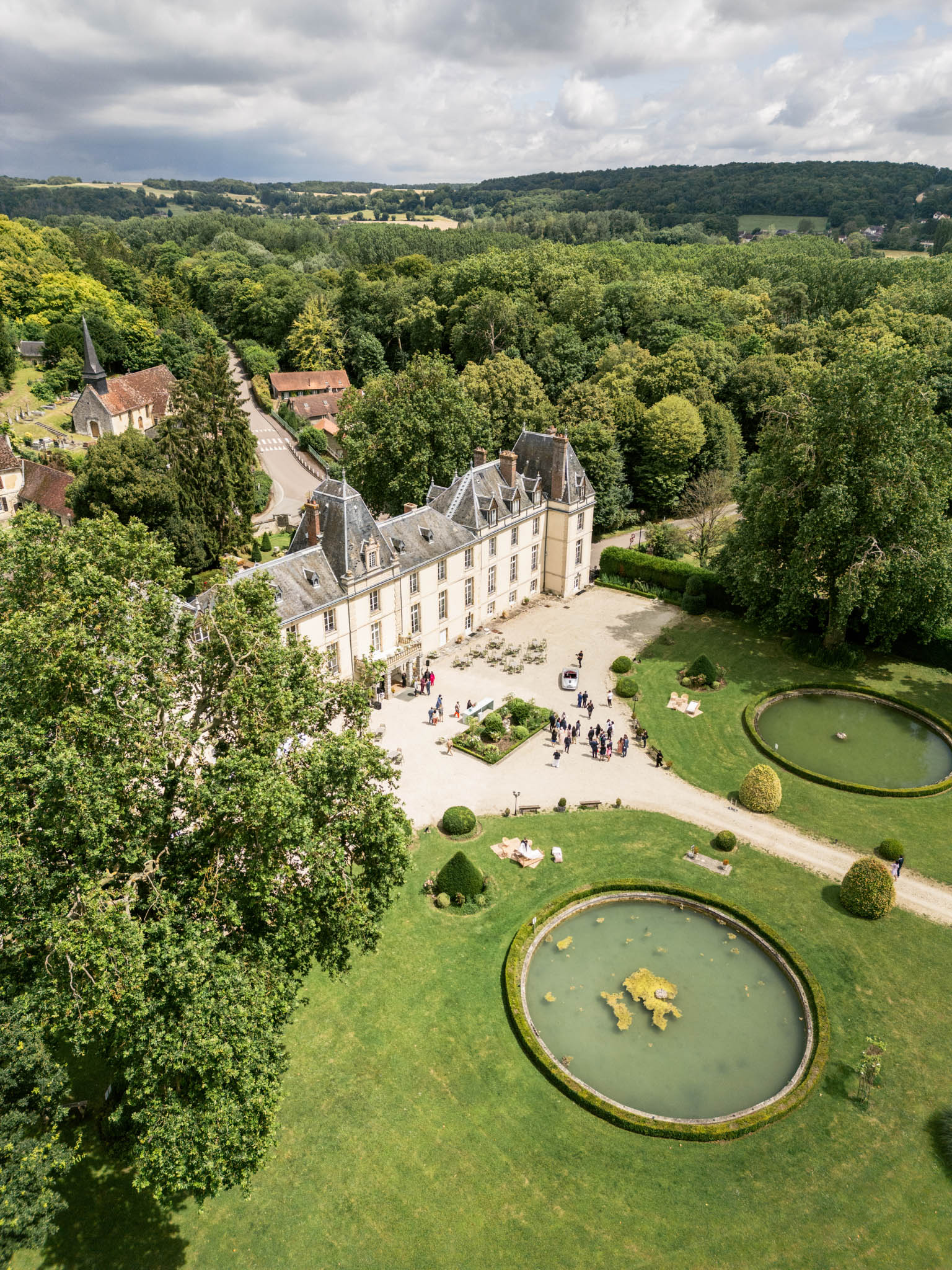 Aerial Renaissance chateau with mansard roof towers formal gardens ornamental ponds and stone church in woodland