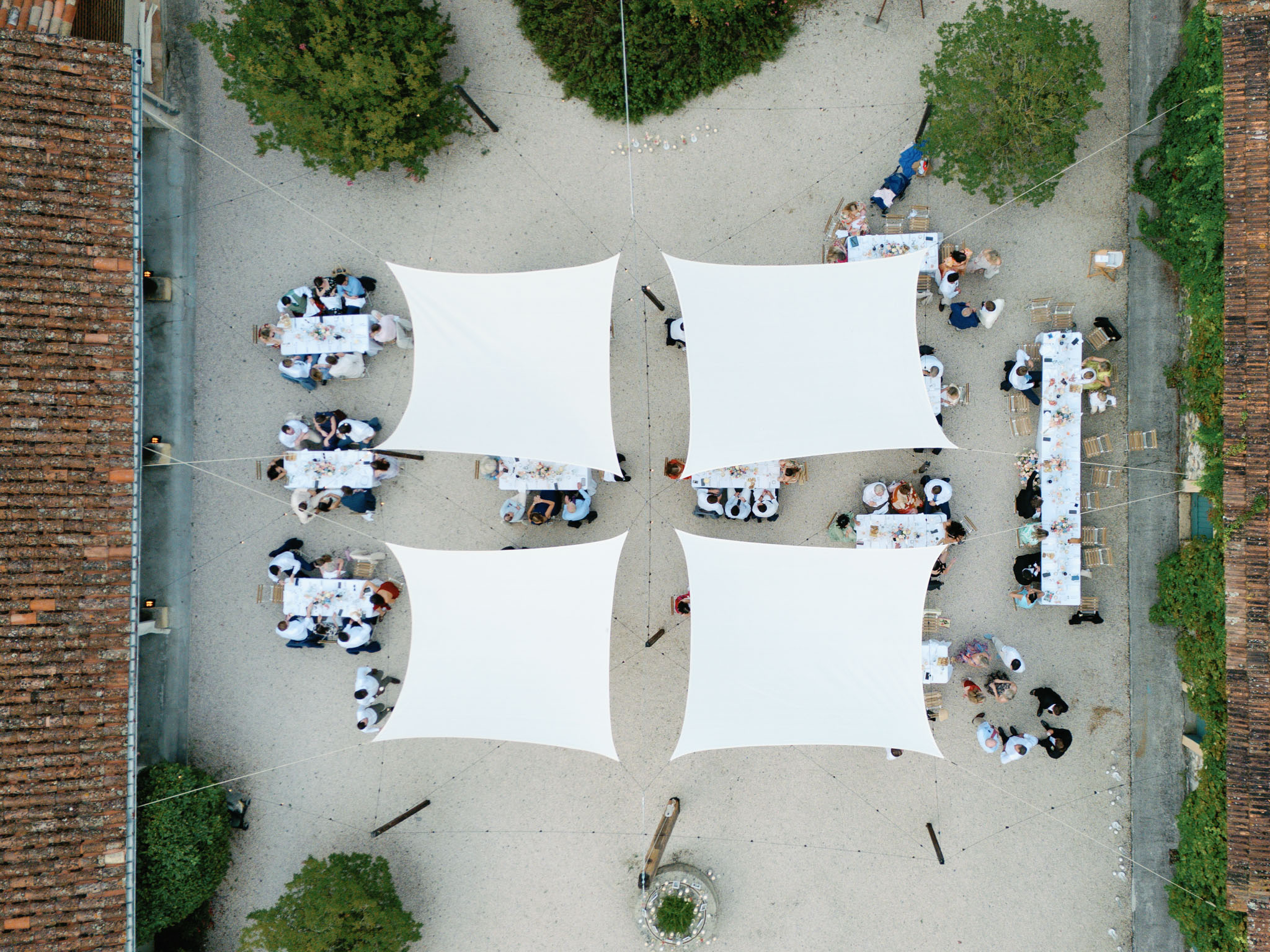 Aerial view of outdoor wedding reception under white sail canopies in a chateau courtyard with long dining tables