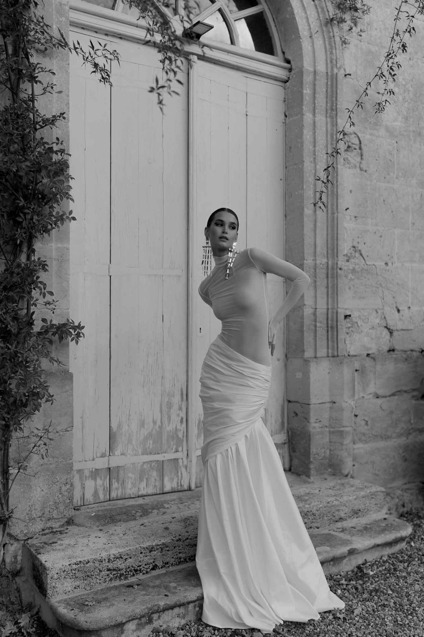 Black and white bride in sheer high-neck ruched mermaid gown with chandelier earrings on stone steps