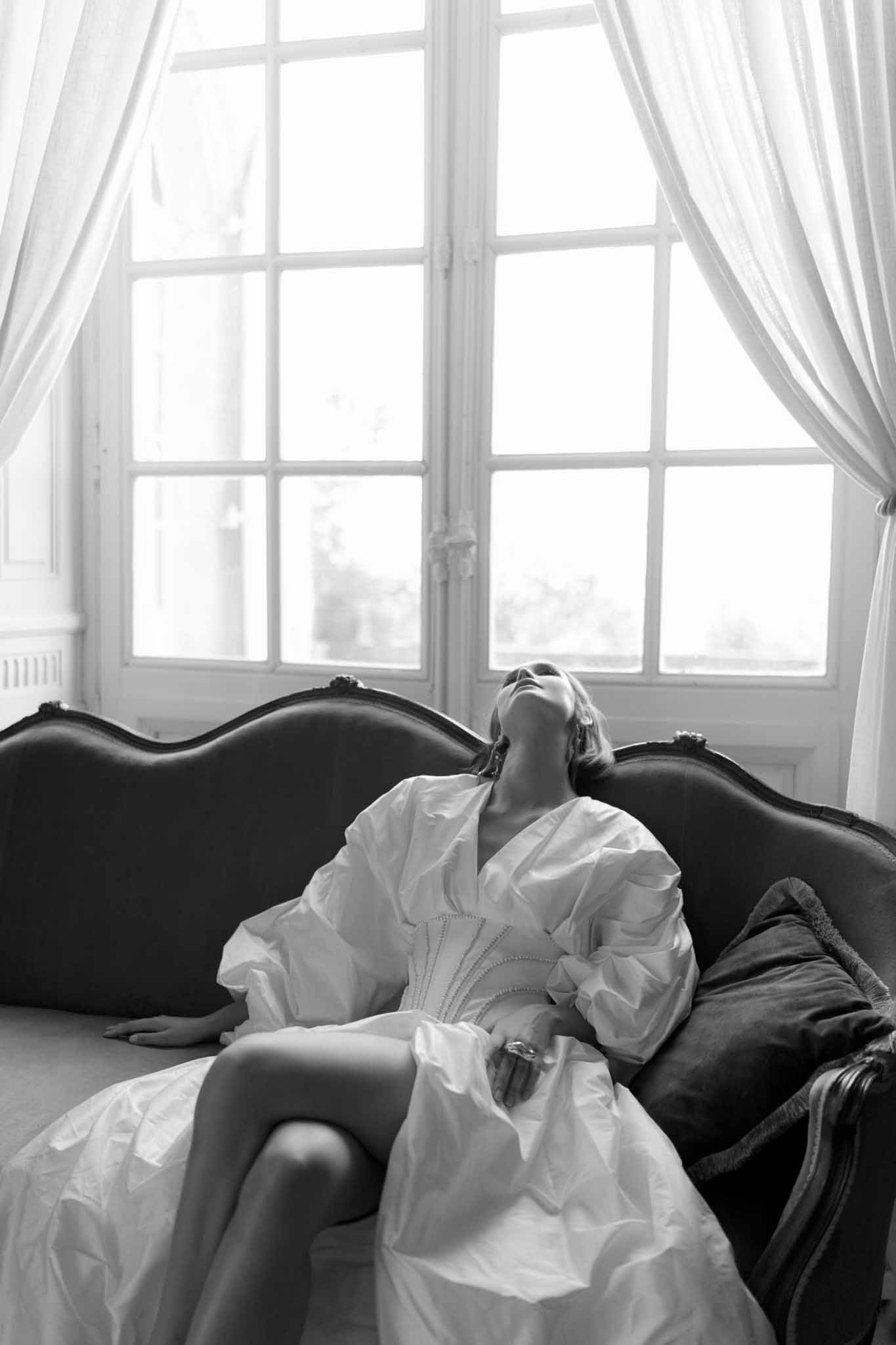 Black and white bride in bishop-sleeve gown reclining on Louis XVI canape beside French windows