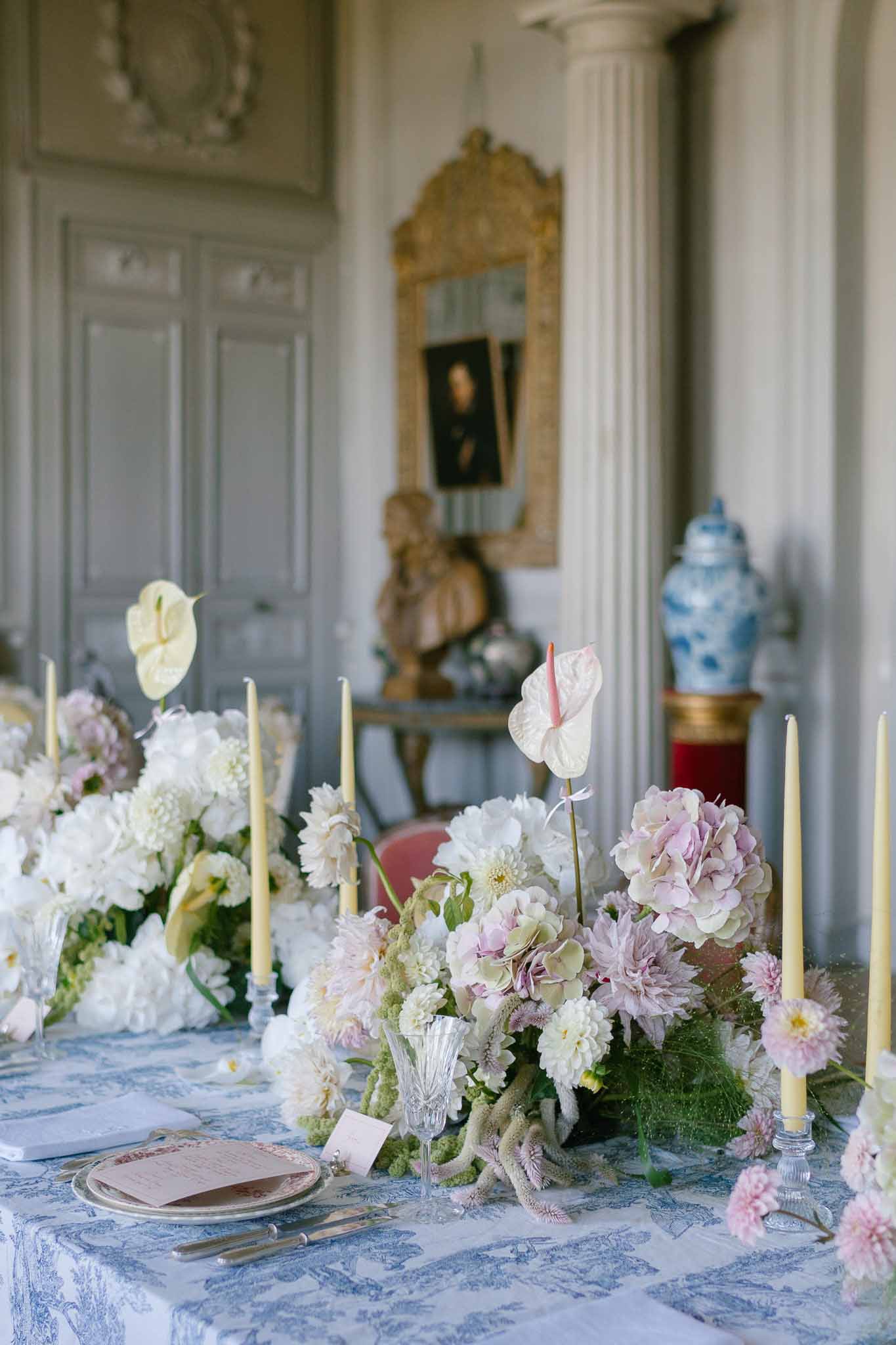 Toile tablecloth with pink dahlias, mauve hydrangeas, yellow taper candles, and blue-white ginger jar decor