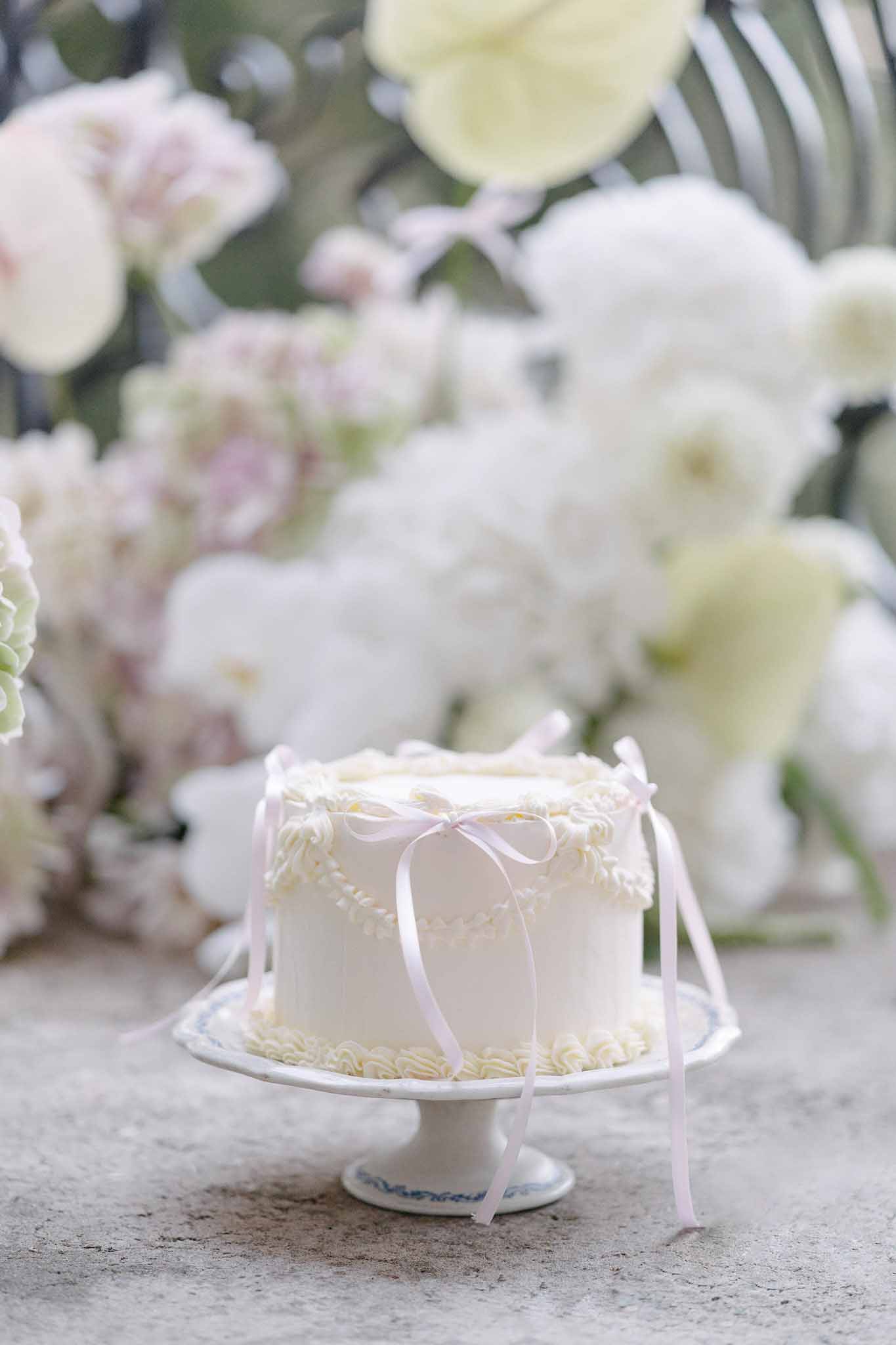 Single-tier ivory fondant cake with buttercream borders and pink ribbon bows on white pedestal stand