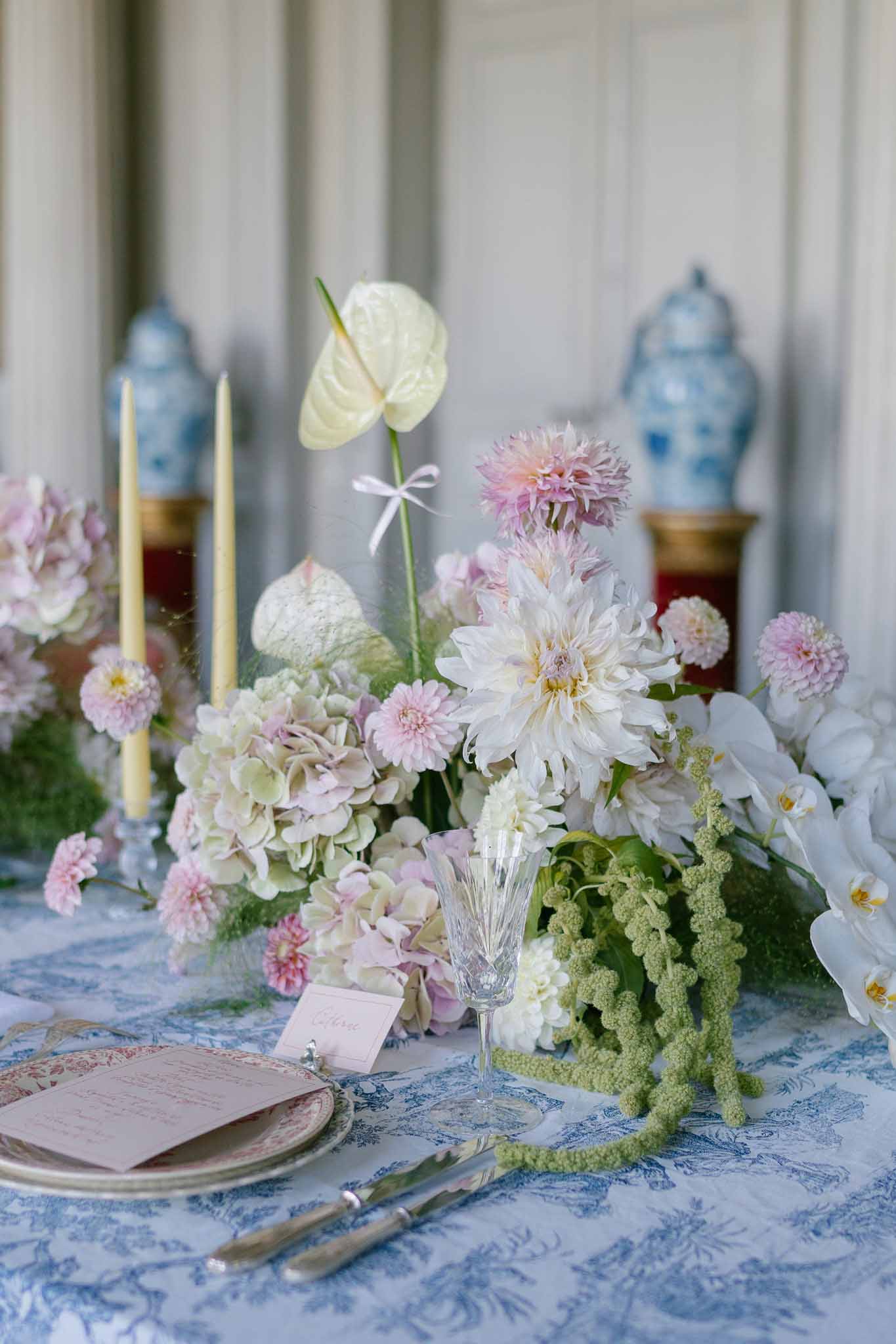 Place setting with toile de Jouy linen, red china plate, dahlias, orchids, and chinoiserie ginger jars