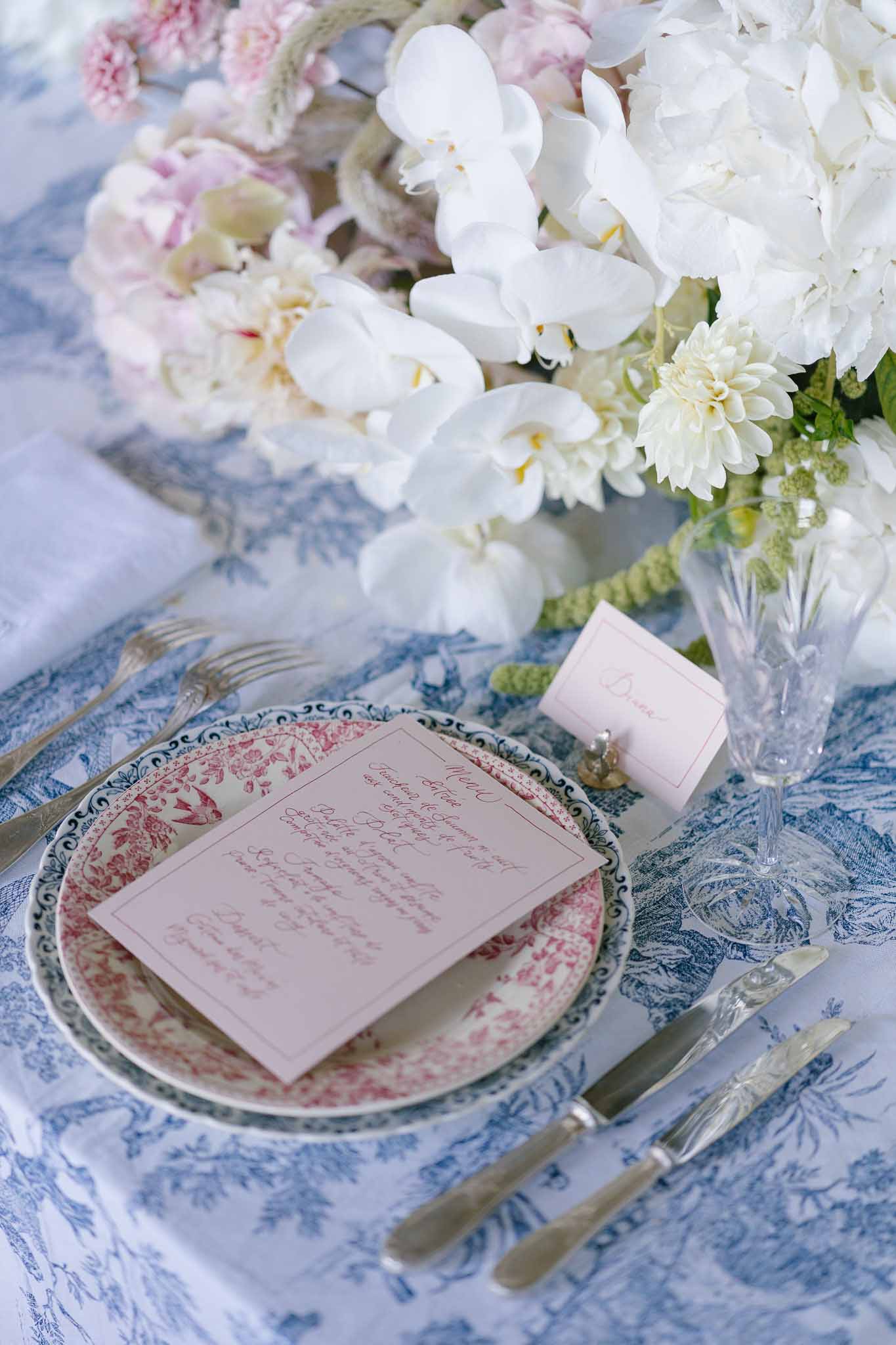 Blue toile plate on navy charger with blush menu card beside white orchid and hydrangea centerpiece