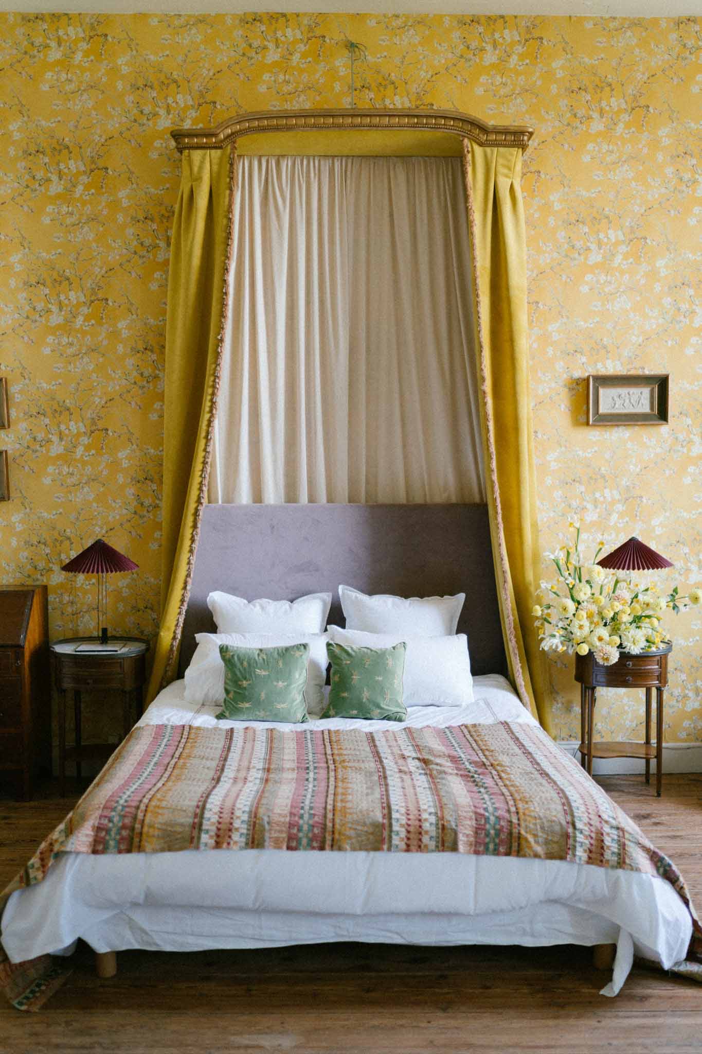 Chateau bedroom with gilt crown canopy, mustard velvet drapes, yellow floral wallpaper, and narcissus