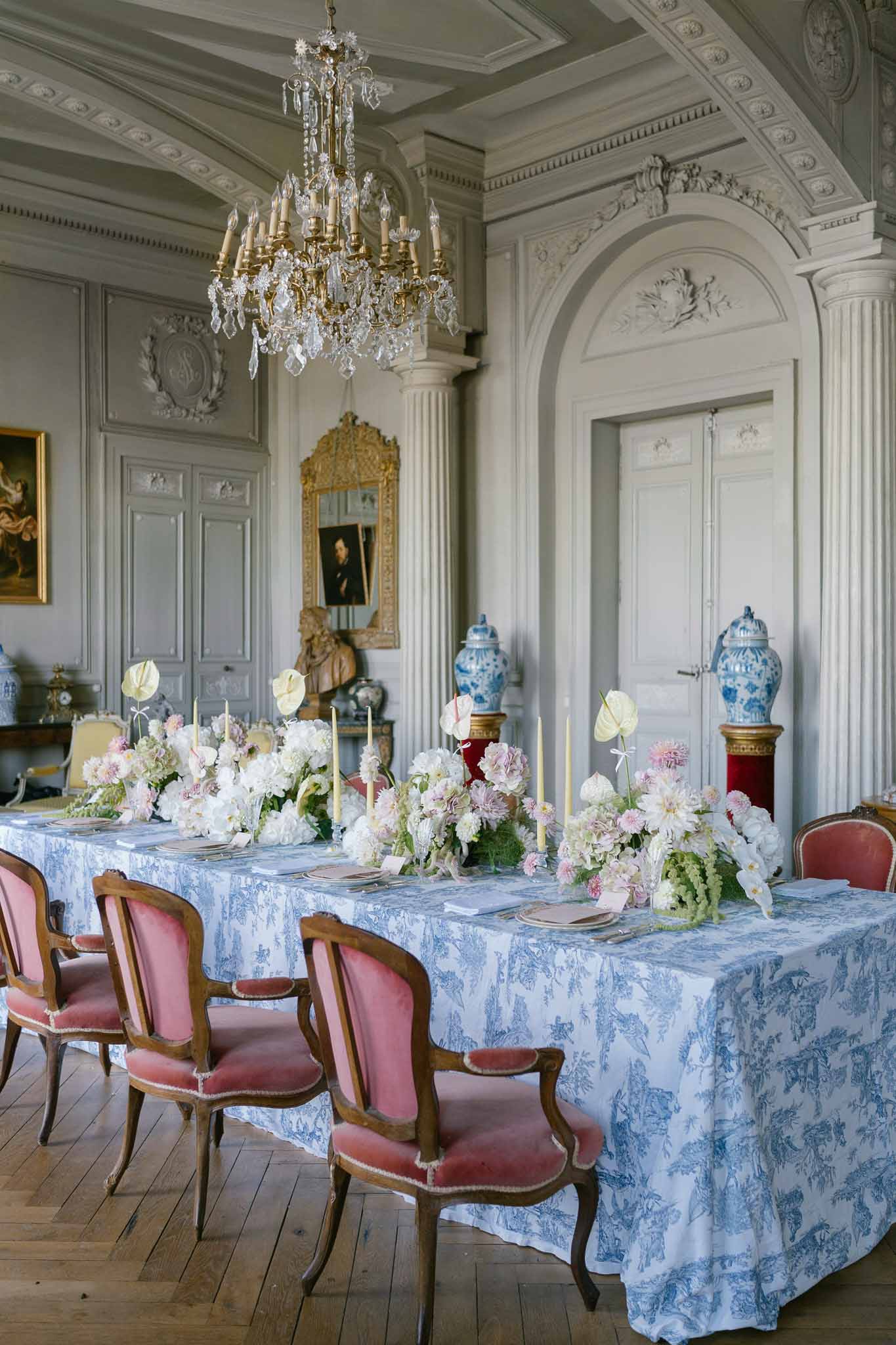Reception table with toile de Jouy cloth, dahlia floral runner, and gold candle holders in chateau paneled dining room