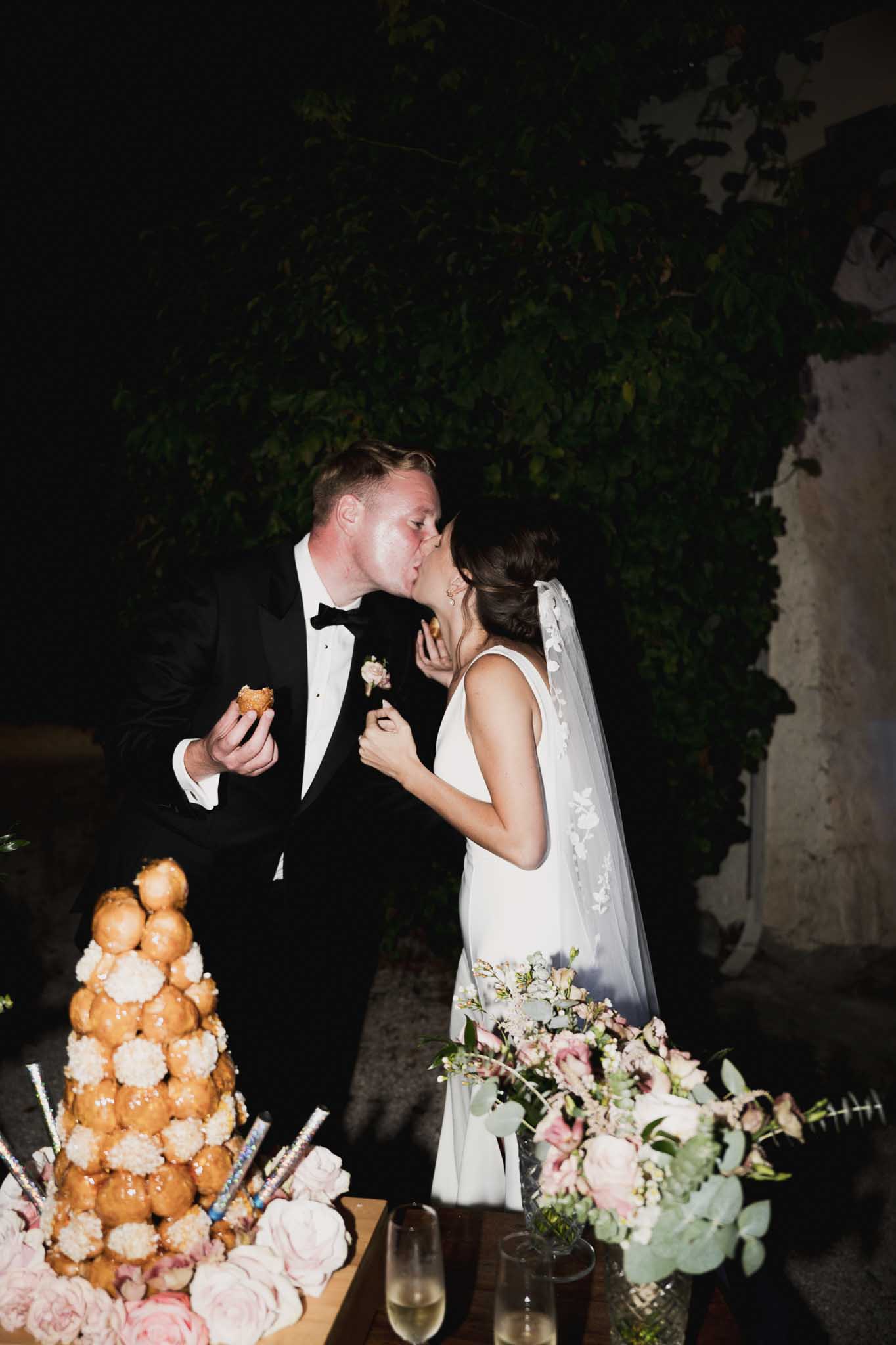 Bride and groom sharing dessert moment with croquembouche at outdoor garden reception