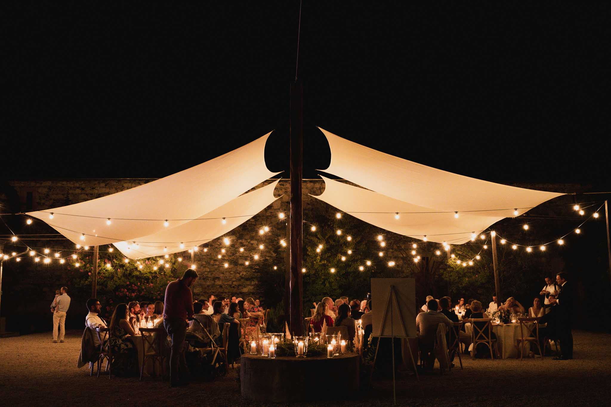 Evening reception under tented canopy with string lights and guests dining at outdoor courtyard venue