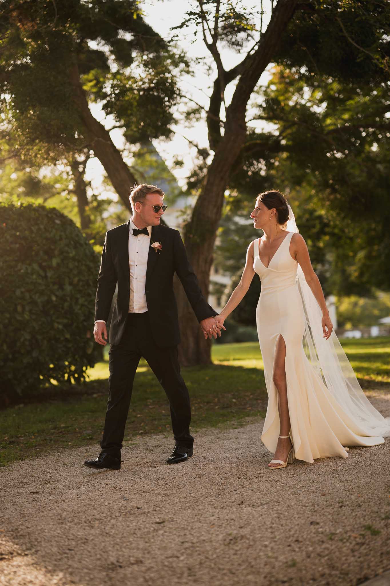 Bride and groom walking hand-in-hand through manicured garden pathway