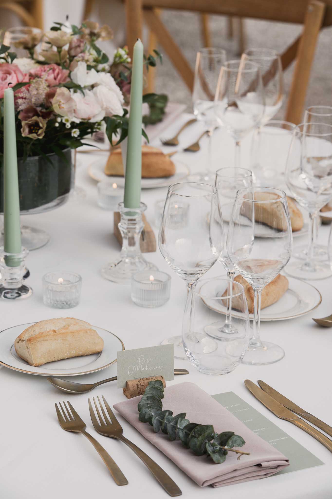 Reception table setting with gold-rimmed plates, sage and pink napkins, and peony centerpiece at wedding venue