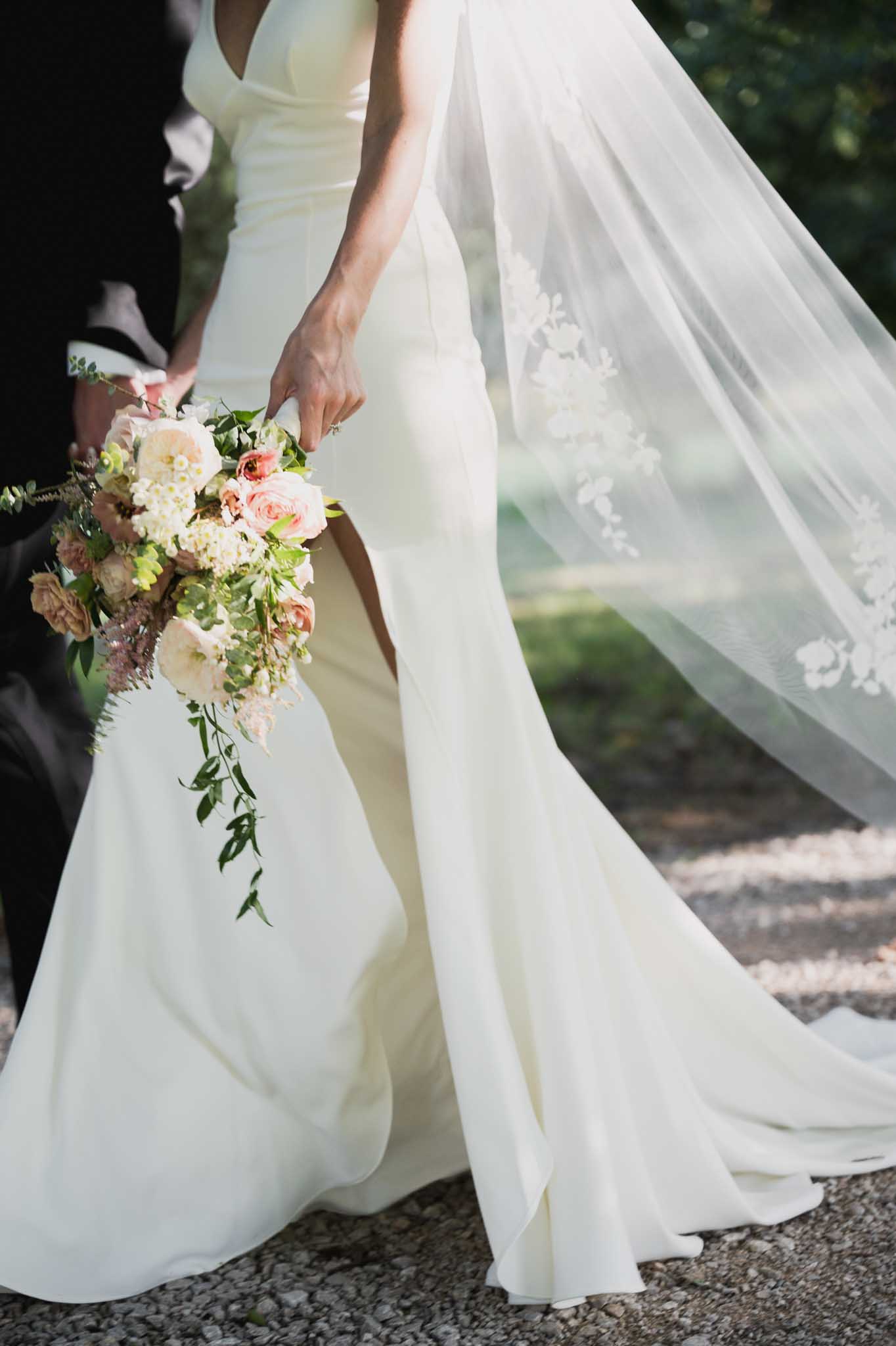 Bride holding bouquet during outdoor wedding ceremony with groom partially visible
