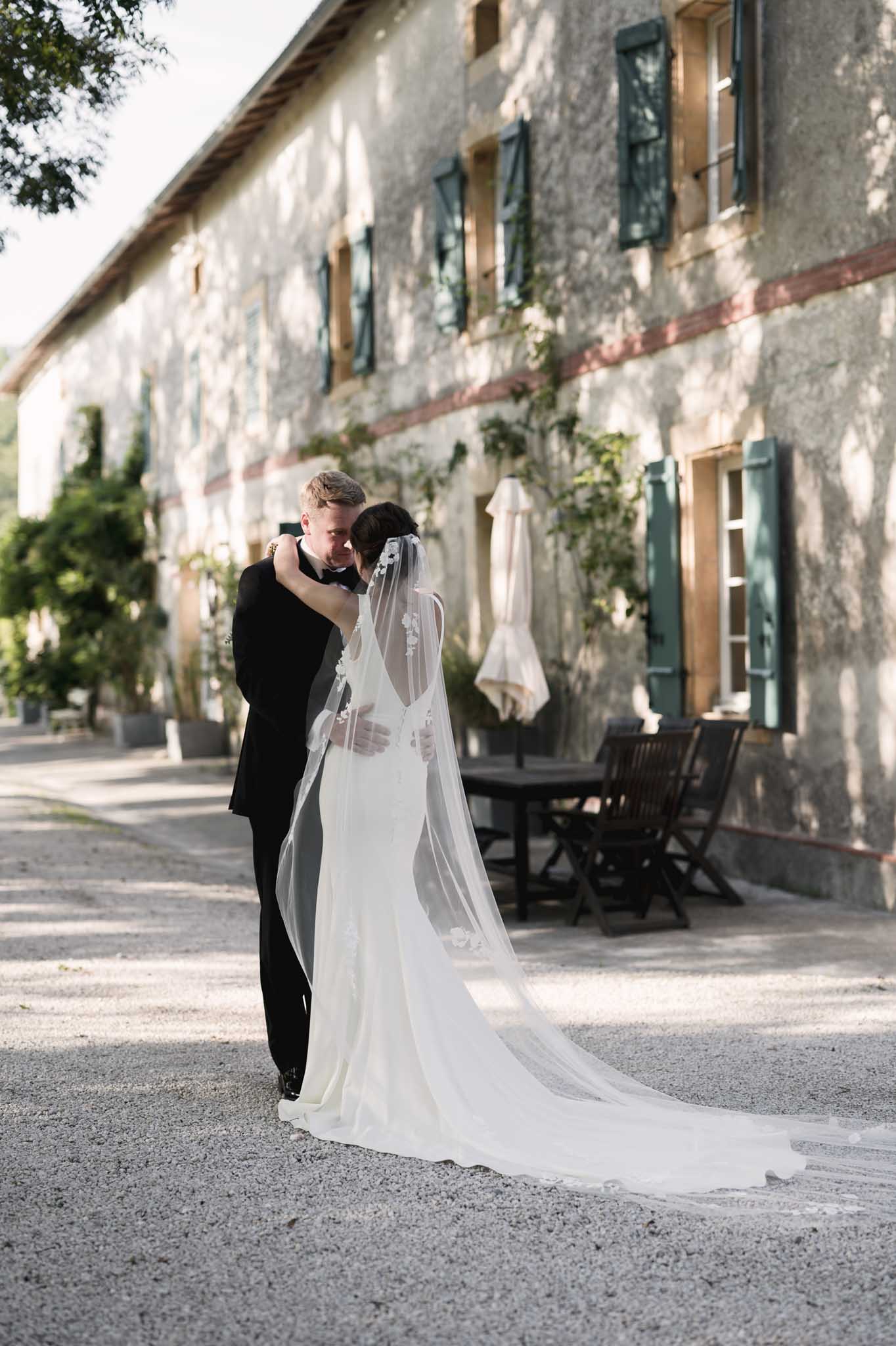 Groom carrying bride in courtyard of historic stone building with green shutters